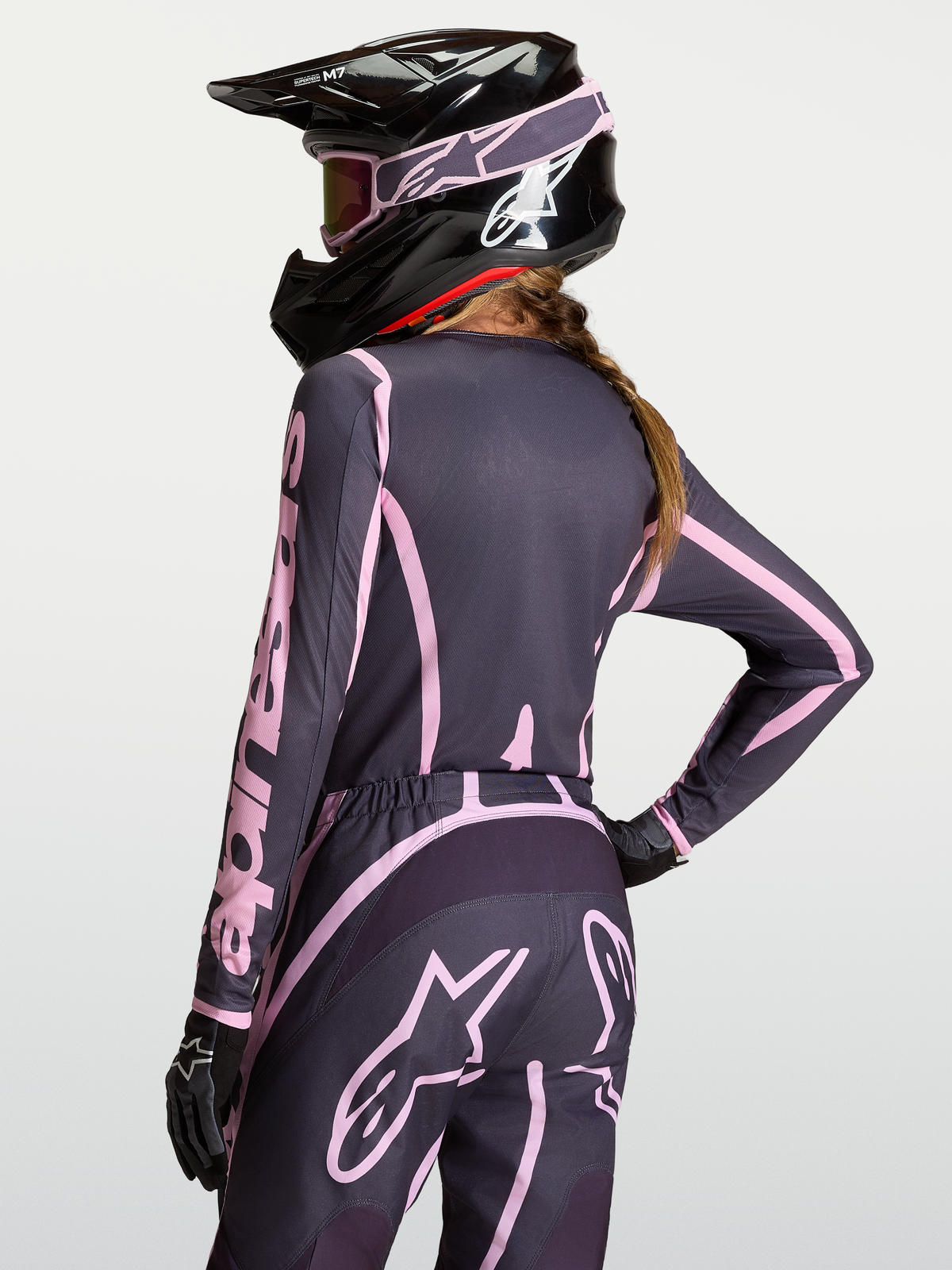 Alpinestars Stella Fluid Apex V2 Jersey, women's motocross gear in Graystone and Old Pink, moisture-wicking polyfabric with extended rear cut for coverage, shown on-model with matching pants and black helmet.