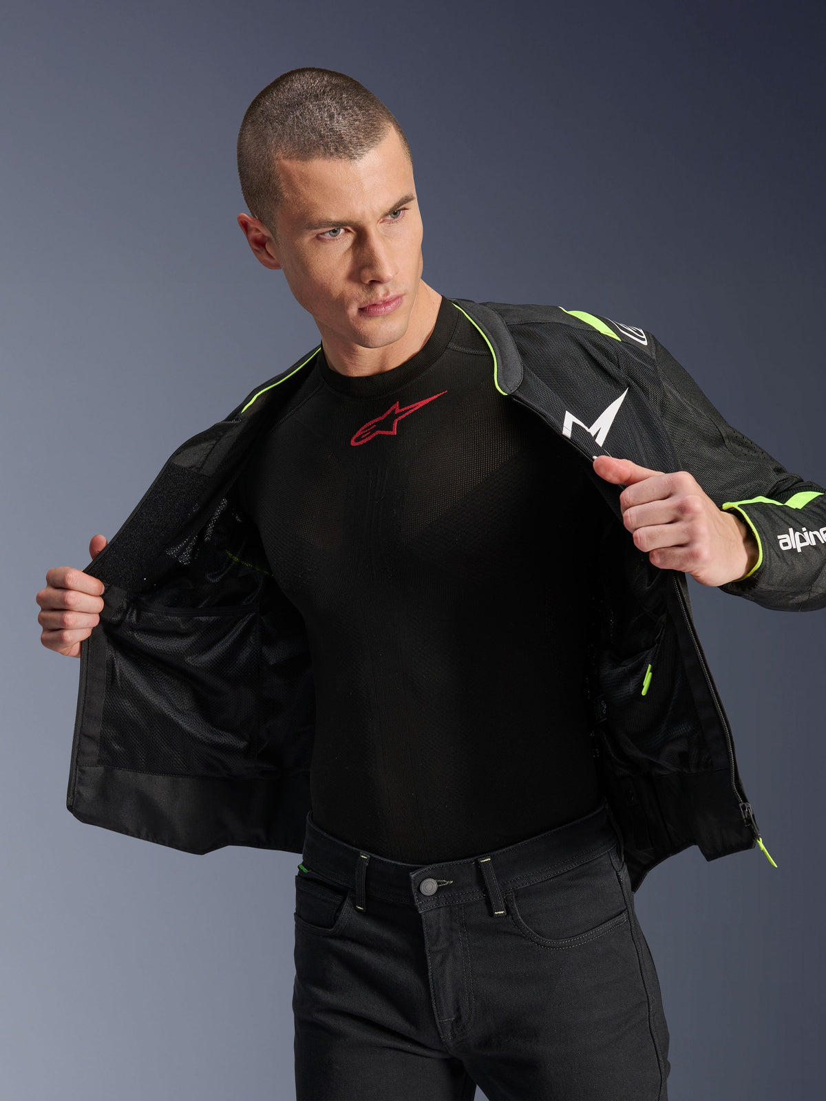 Male model wearing the Alpinestars T-Sps Air V2 Jacket in Black and Yellow Fluo, shown open to highlight the internal mesh construction and pocketing, paired with a black Alpinestars base layer and black pants, urban motorcycle riding gear style