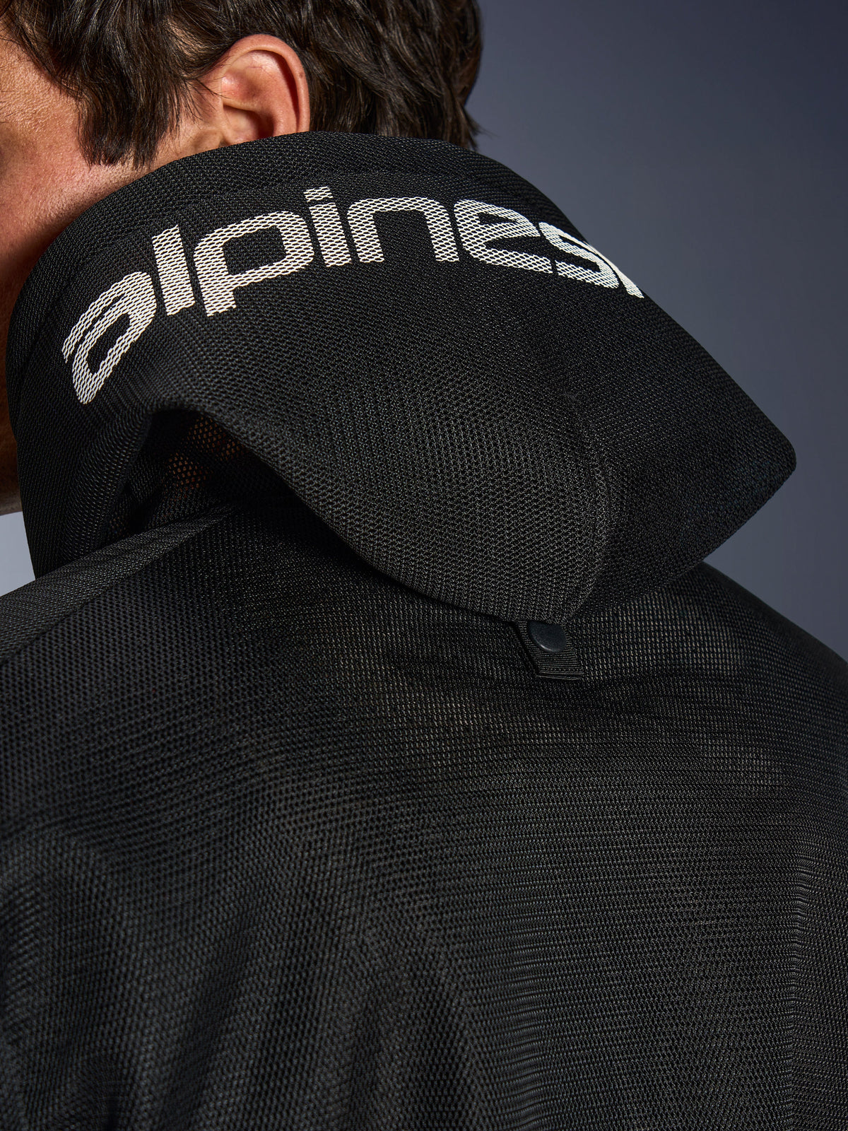 Alpinestars Chrome Superairflow Hoodie, Black, Detail view of the 3D mesh hood with white alpinestars branding across the top, showing the rear stabilization snap button, ventilated textile motorcycle gear for extreme heat
