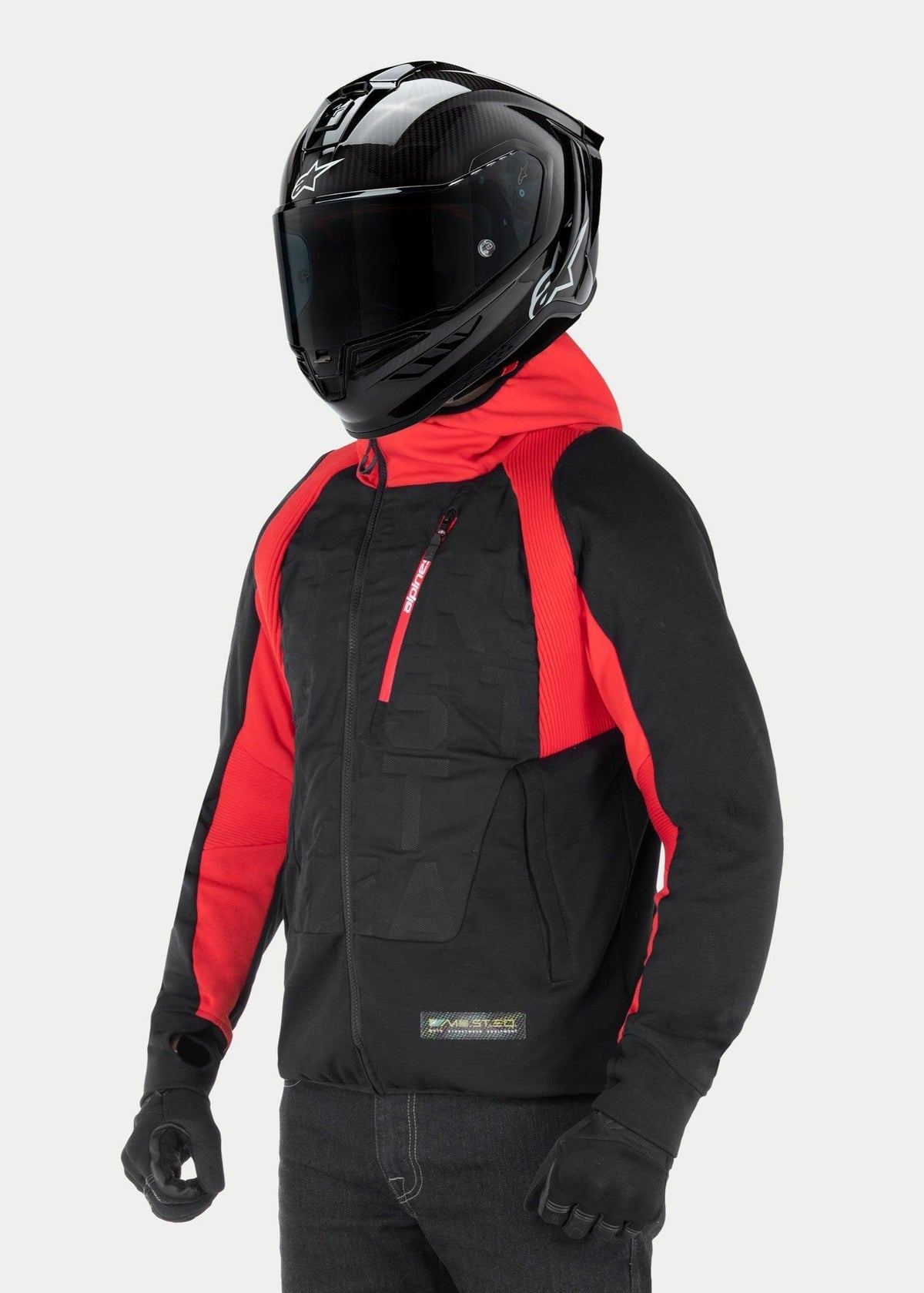 Alpinestars MO.ST.EQ Hybrid Hooded Jacket, Urban Motorcycle Hoodie, Black and Red, featuring an angled front zipper and ribbed shoulder panels, worn with a black full-face helmet and black gloves, contemporary streetwear style