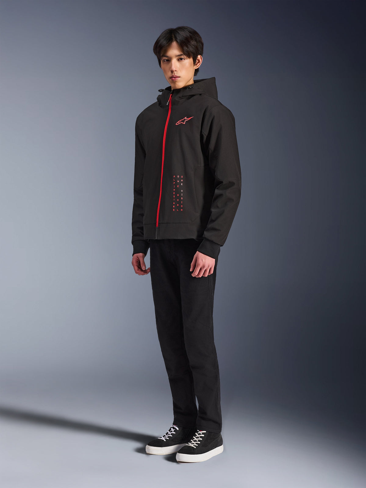 Alpinestars Radium Tech Hoodie, Black Bright Red, urban riding technical hoodie featuring a red front zipper and chest logo, worn by a model with black pants and black sneakers with white soles, full-body studio shot