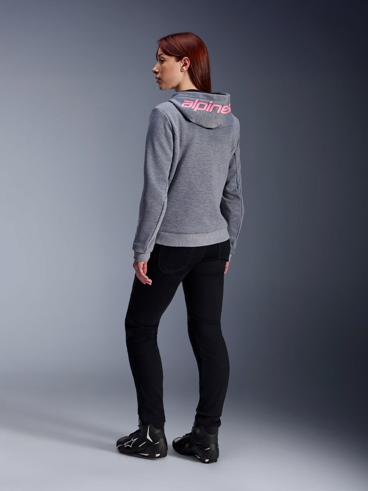 Alpinestars Stella Chrome V2 Sport Hoodie, Women's Motorcycle Hoodie, Gray Heather with Pink Fluo branding on hood, back view, worn with black pants and riding shoes, casual urban street style with motorcycle protection