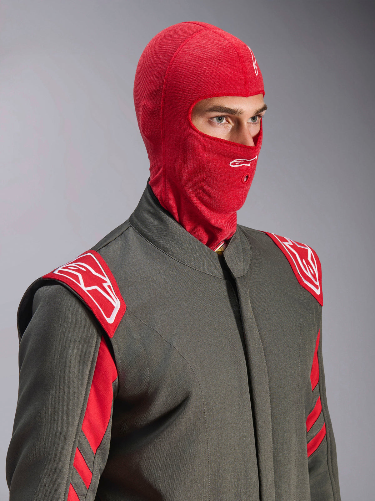 Alpinestars ZX Evo V3 Balaclava, Red, worn by a driver in a gray racing suit with red and white accents, featuring a white Astars logo on the forehead and a hydration tube port, flame-resistant base layer for auto racing