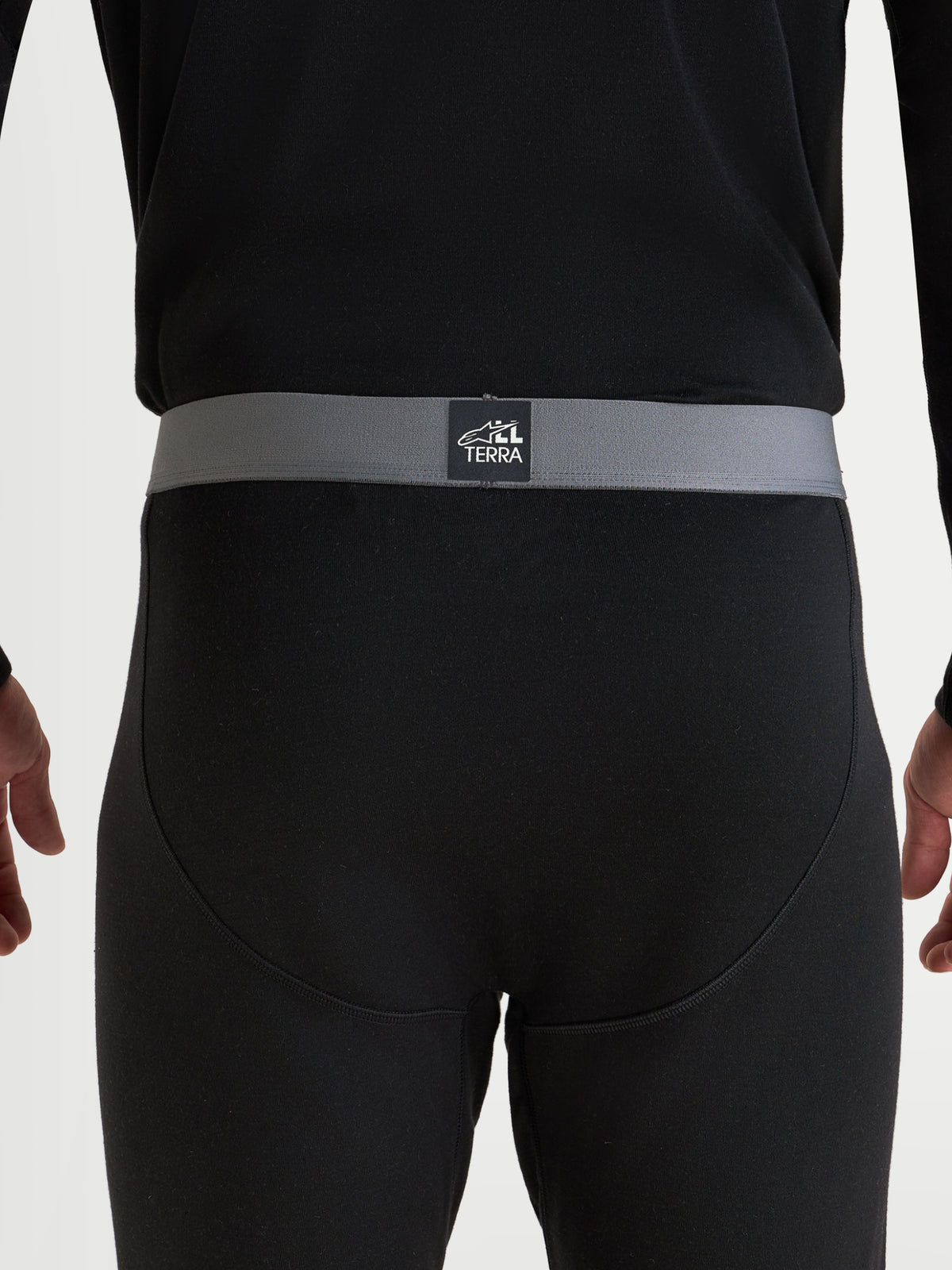 Alpinestars AT-8 Merino Bottom Tech Layer, men's adventure touring motorcycle base layer in black, close-up back view showing the grey elasticated waistband with All Terra branding and seamless construction