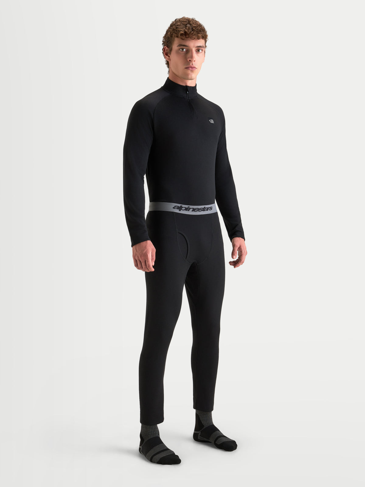 Alpinestars AT-8 Merino Bottom Tech Layer, men's motorcycle thermal base layer pants in black, on-model front view showing elasticated waistband with branding and seamless merino wool blend construction.
