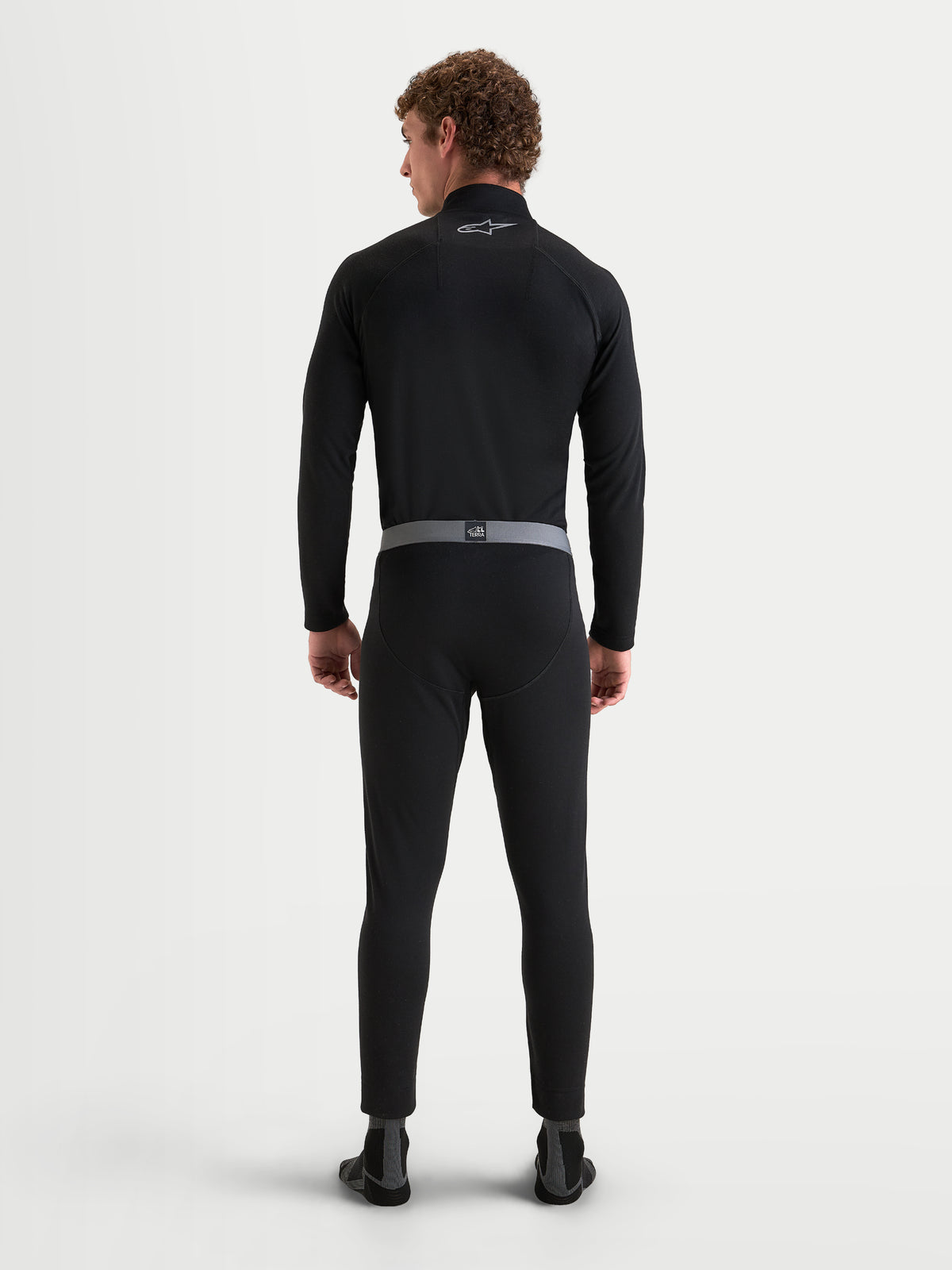 Alpinestars AT-8 Merino Bottom Tech Layer, men's motorcycle base layer pants in black with grey elasticated waistband, rear view on a model wearing matching long sleeve top and thermal bottoms, merino wool blend adventure touring riding apparel
