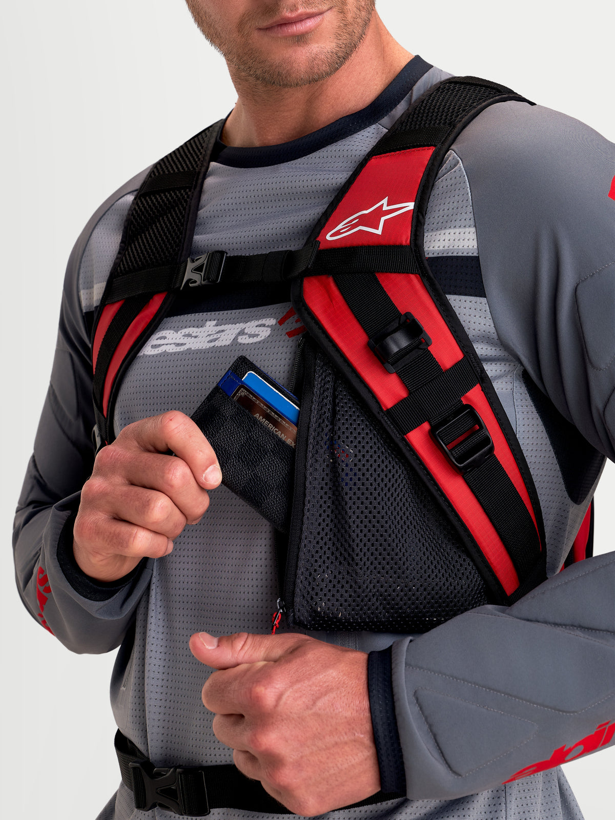 Alpinestars AT-9 Backpack, motocross backpack, black and bright red, close-up view showing the padded shoulder harness system and zippered mesh accessory pocket worn by a model