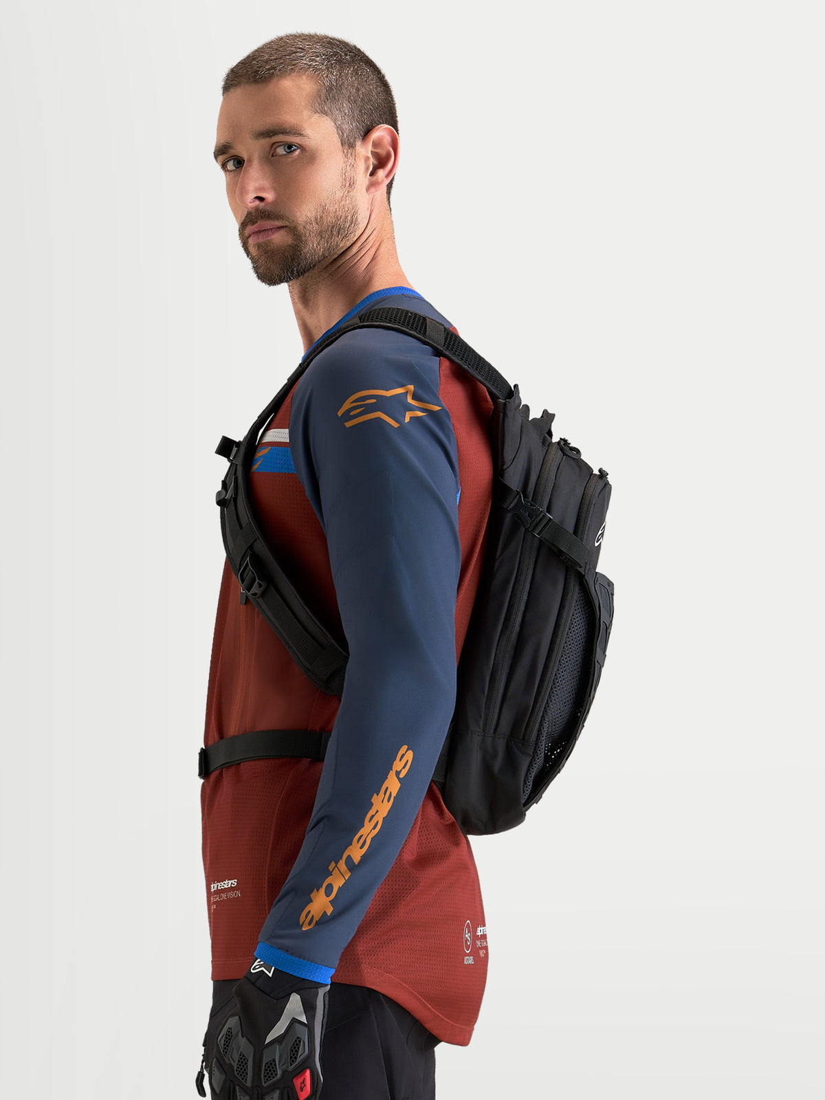 Alpinestars AT-9 Backpack, motocross and everyday utility backpack in black, side profile view worn by a model in riding gear.