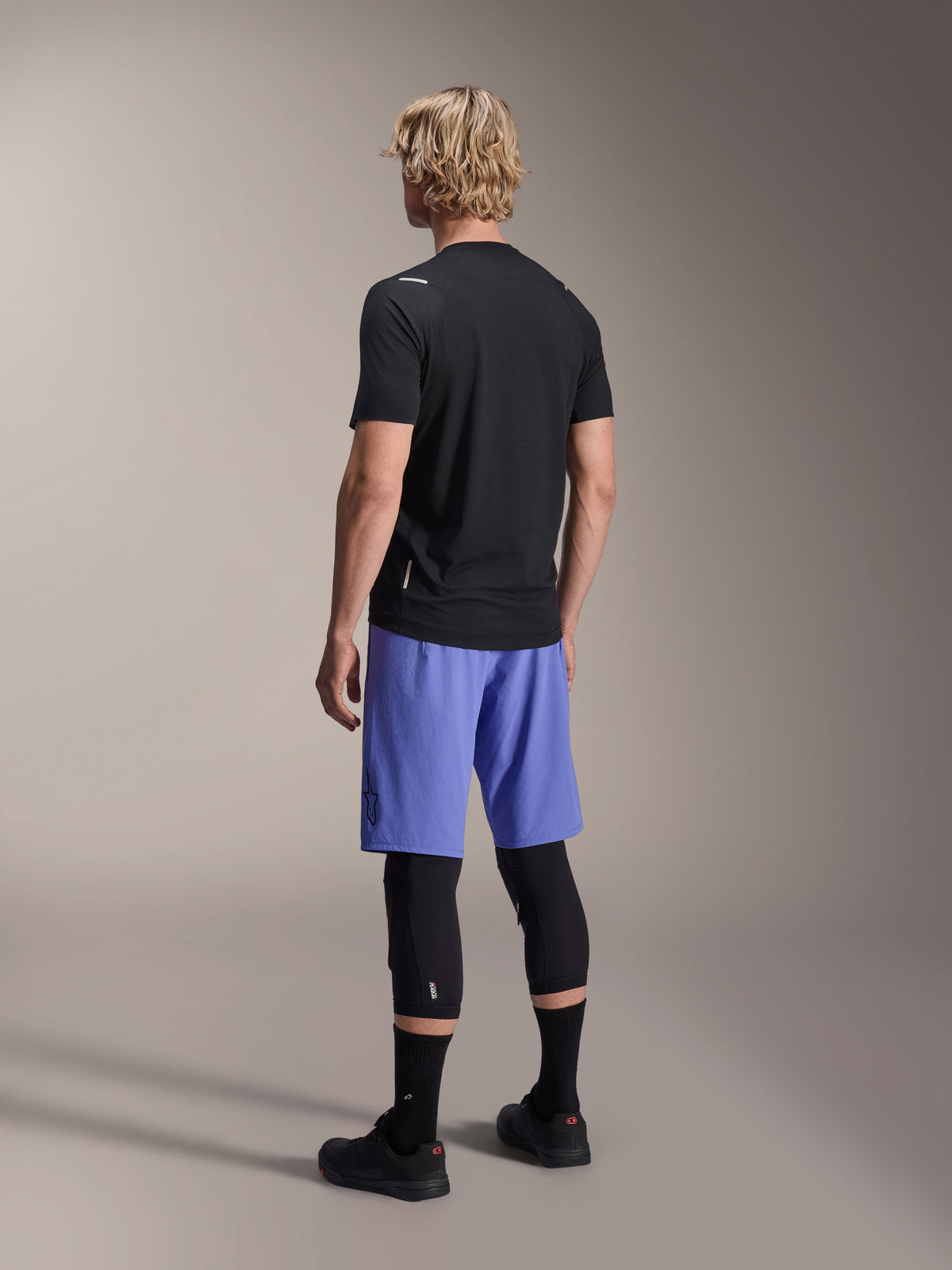 Alpinestars A-Aria Switch Jersey, Short Sleeve MTB Jersey, Black, rear view on model wearing blue shorts and black knee guards, performance cycling gear for trail riding
