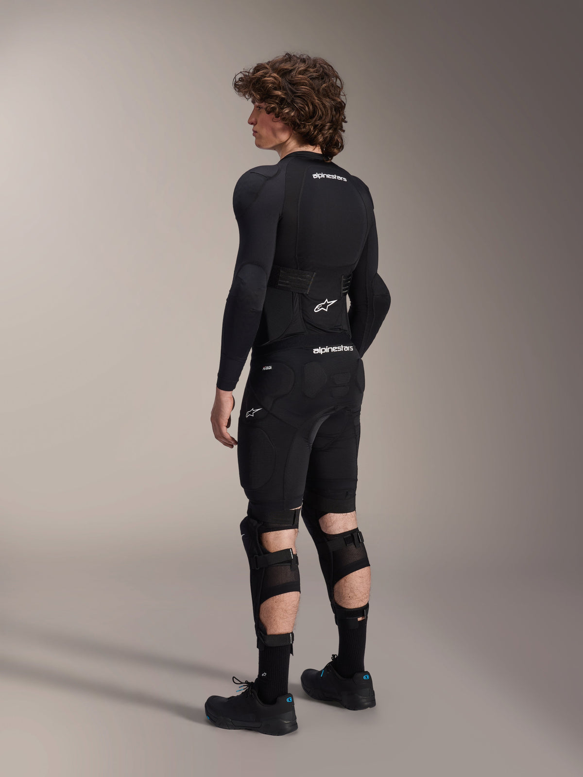 Alpinestars A-Impact Plasma Protection Jacket - Long Sleeve, Black with white logos, back view on a model showing integrated back protector, breathable mesh chassis, paired with mountain bike protective shorts and knee guards