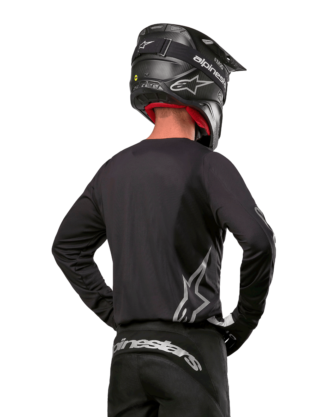 Motocross rider viewed from the back wearing the Alpinestars 2024 Fluid Graphite Jersey in Black Silver, featuring a large silver logo on the side, paired with a black carbon-texture helmet and black pants, professional off-road racing gear