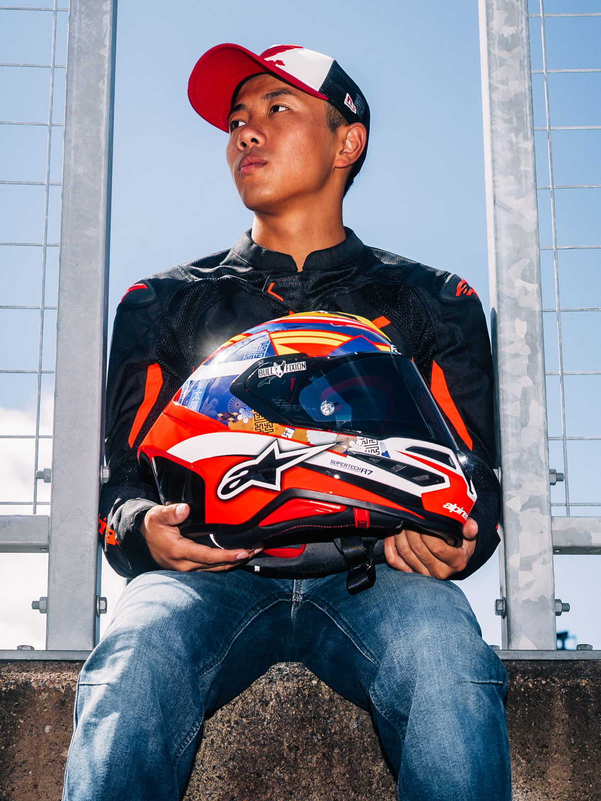 Alpinestars S-R7 Taiyo Furusato Helmet, Full Face Motorcycle Racing Helmet, Red, White, and Blue Graphic, held by rider Taiyo Furusato wearing a black jacket, outdoor trackside view.