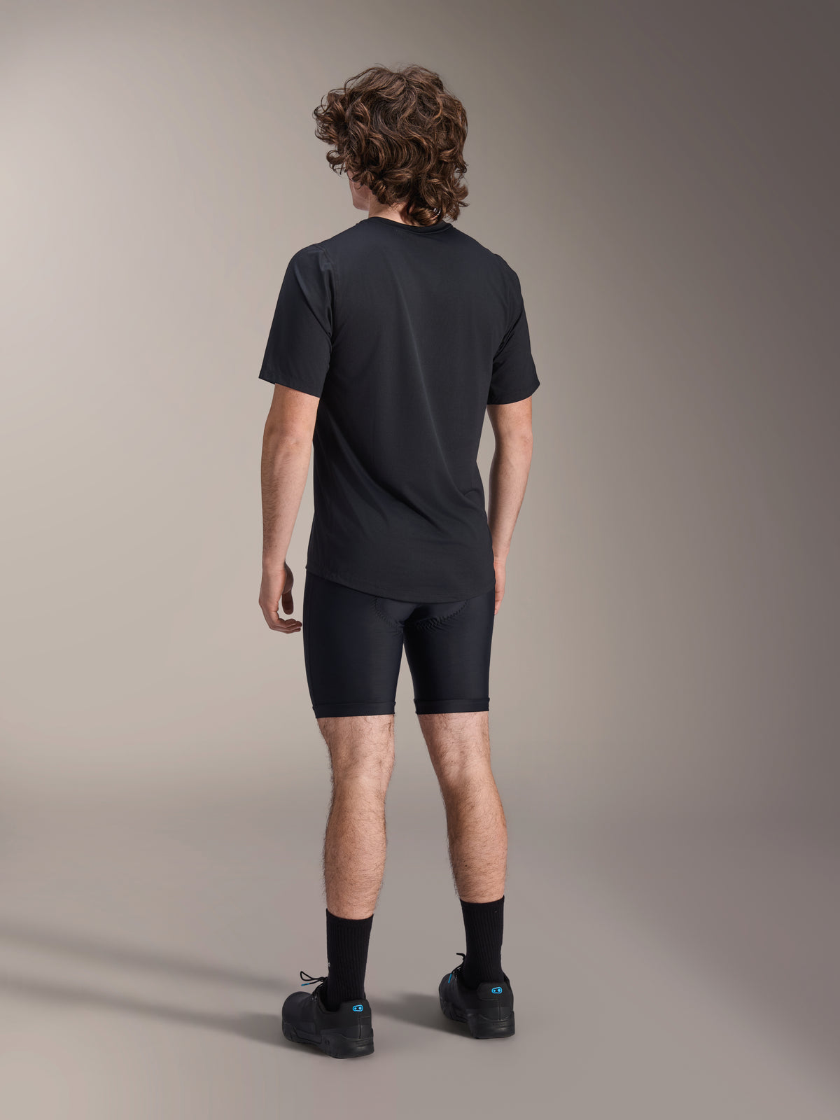 Alpinestars A-Dura Liner Shorts, Black Cycling Liner Shorts, back view on model, tight-fitting stretch fabric with visible chamois padding seams, paired with a black t-shirt and cycling shoes, mountain bike apparel