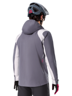 Alpinestars A-Dura Rain Jacket, Mountain Bike Jacket, Dark Titanium Gray, back view featuring light gray shoulder and arm panels, red logo detail on the side, worn with a gray MTB helmet and black and red gloves, technical trail riding apparel