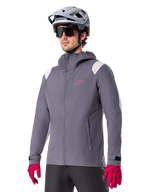 Alpinestars A-Dura Rain Jacket, Mountain Bike Rain Jacket, Dark Titanium Gray with pink logo and white shoulder accents, hooded design with front pockets, worn with pink gloves and a light gray cycling helmet