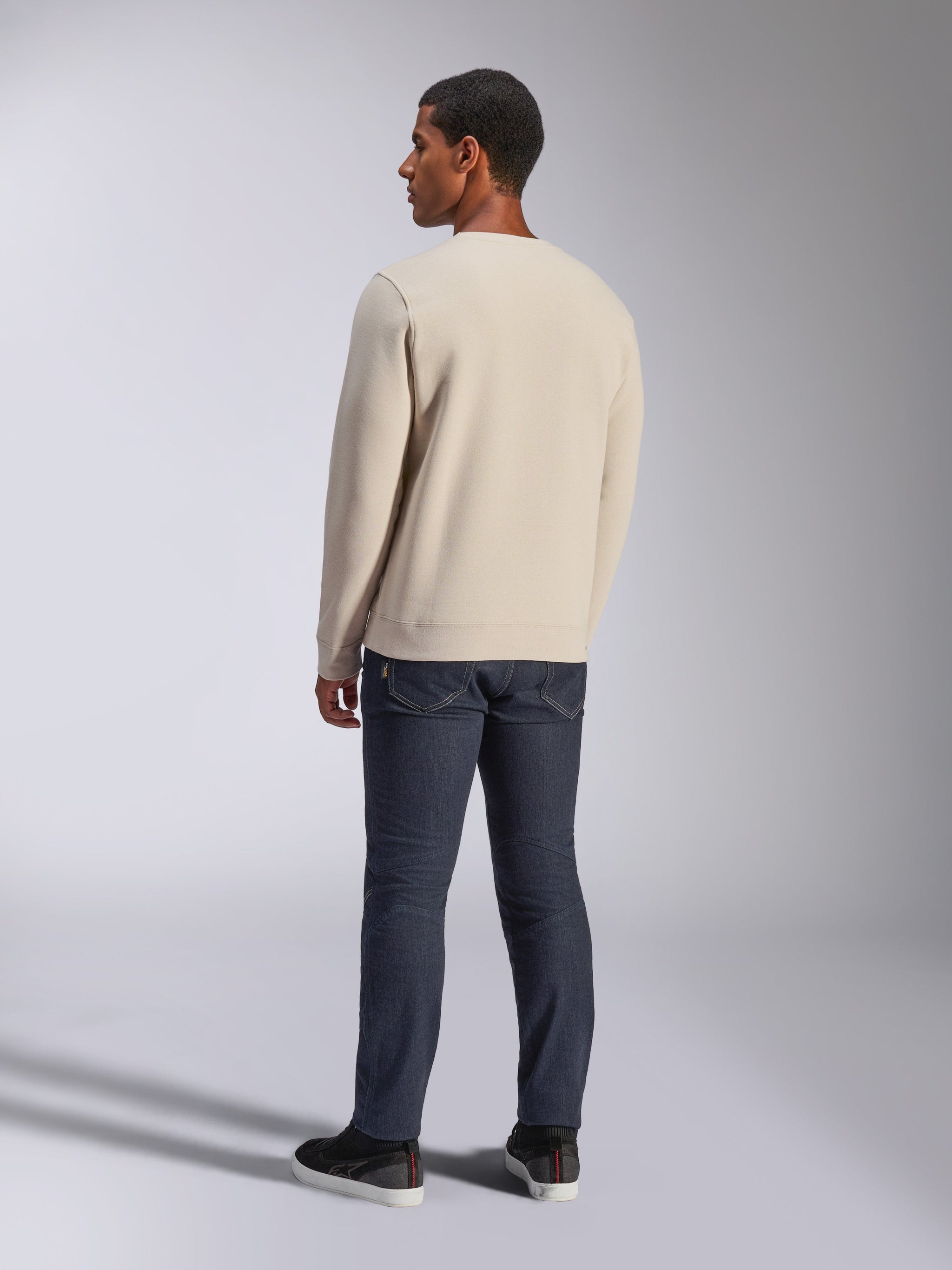 Alpinestars Positive Crew, Off White crewneck sweatshirt, back view on model, paired with dark denim jeans and black sneakers, casual motorsport streetwear, featuring ribbed cuffs and hem