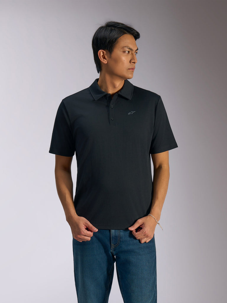 Alpinestars Impetus Sport Polo, Black short-sleeve polo shirt, three-button placket and self collar, small grey Astars logo on the left chest, worn with blue jeans, casual motorsport-inspired sportswear