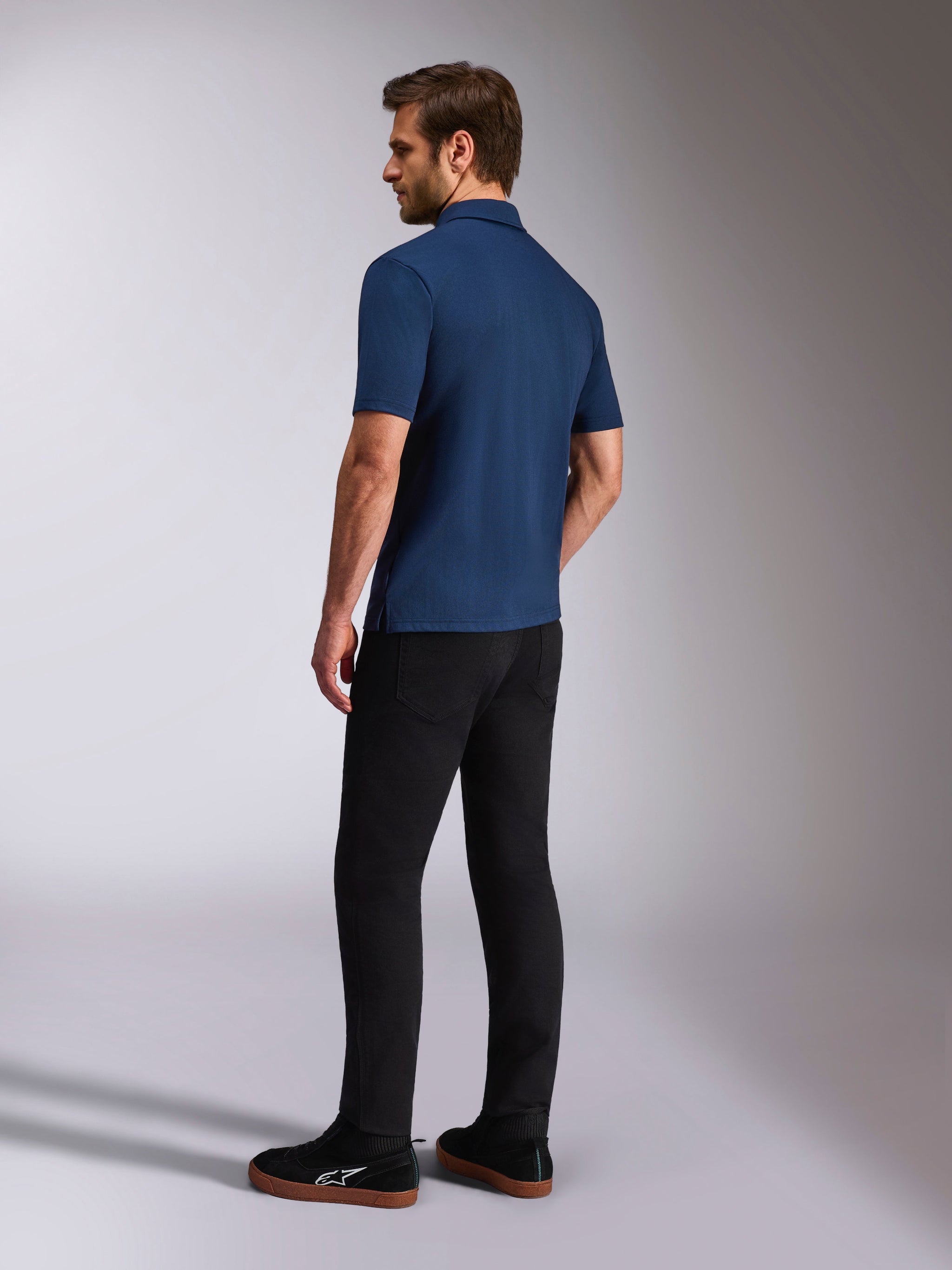 Alpinestars Impetus Sport Polo, Navy Blue Short Sleeve Polo Shirt, Back and side view on model, paired with black pants and black sneakers, casual motorsport lifestyle sportswear