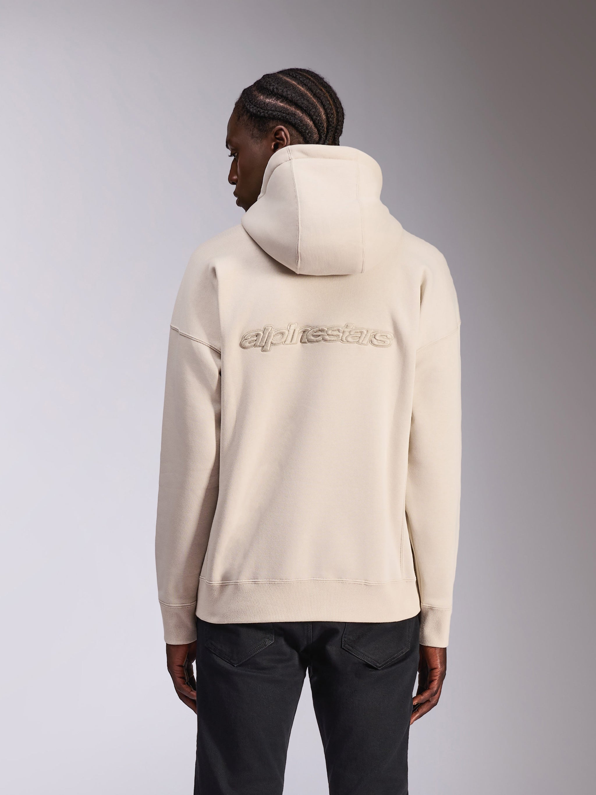 Alpinestars Emergent Oversized Hoodie, casual streetwear, Sand off-white color, featuring 3D embroidered Alpinestars word logo on the back, oversized fit with ribbed hem and cuffs, rear view on model wearing black pants.