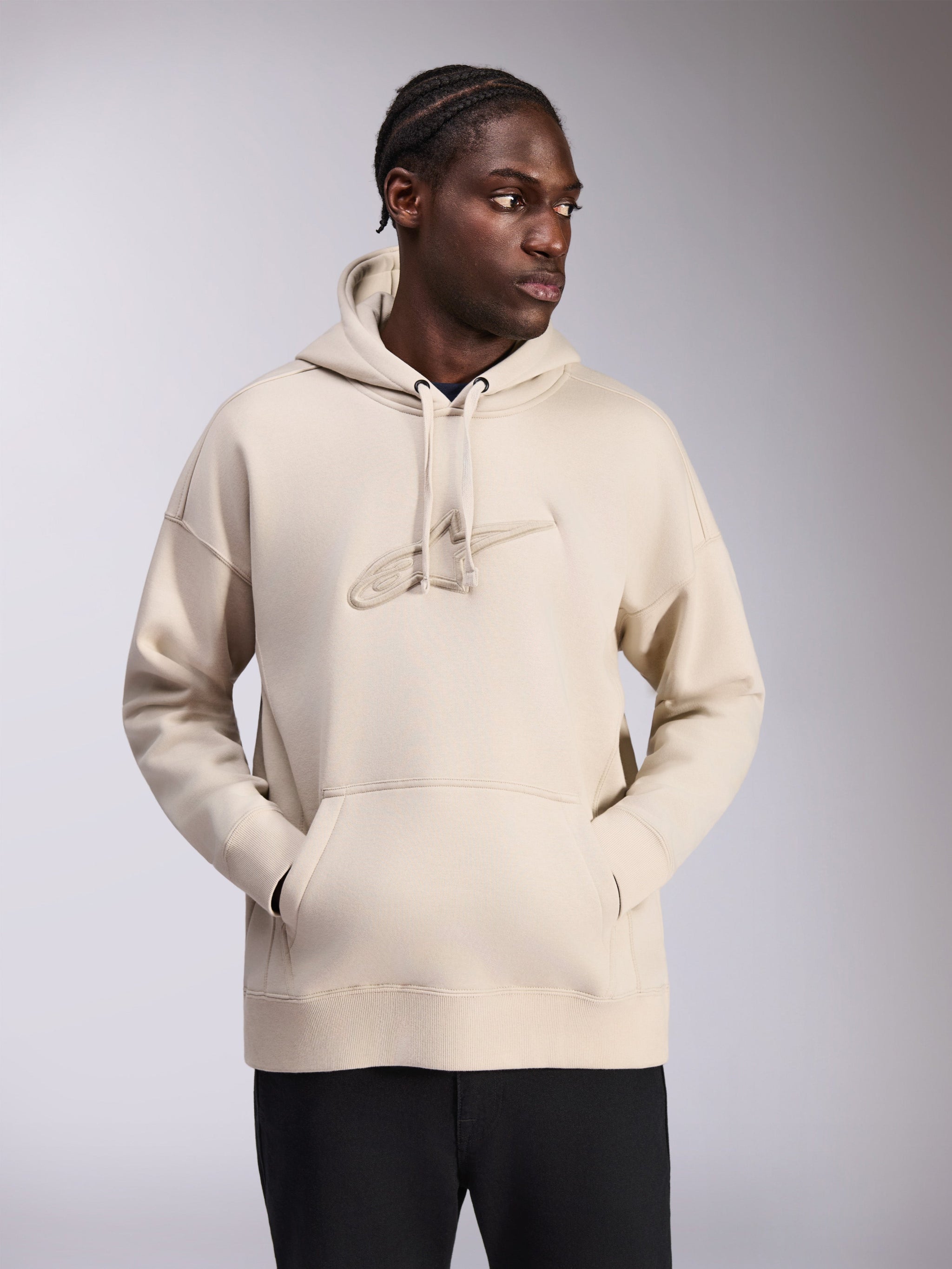 Alpinestars Emergent Oversized Hoodie, Sand color, oversized fit pullover with tonal 3D embroidered Astars logo on chest, kangaroo pocket, drawstring hood, casual streetwear worn by model with black pants.