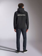 Alpinestars Transverse Hoodie, casual motorsport streetwear, Black with white Alpinestars word logo on the back, long sleeves, ribbed hem and cuffs, worn from behind with dark denim jeans