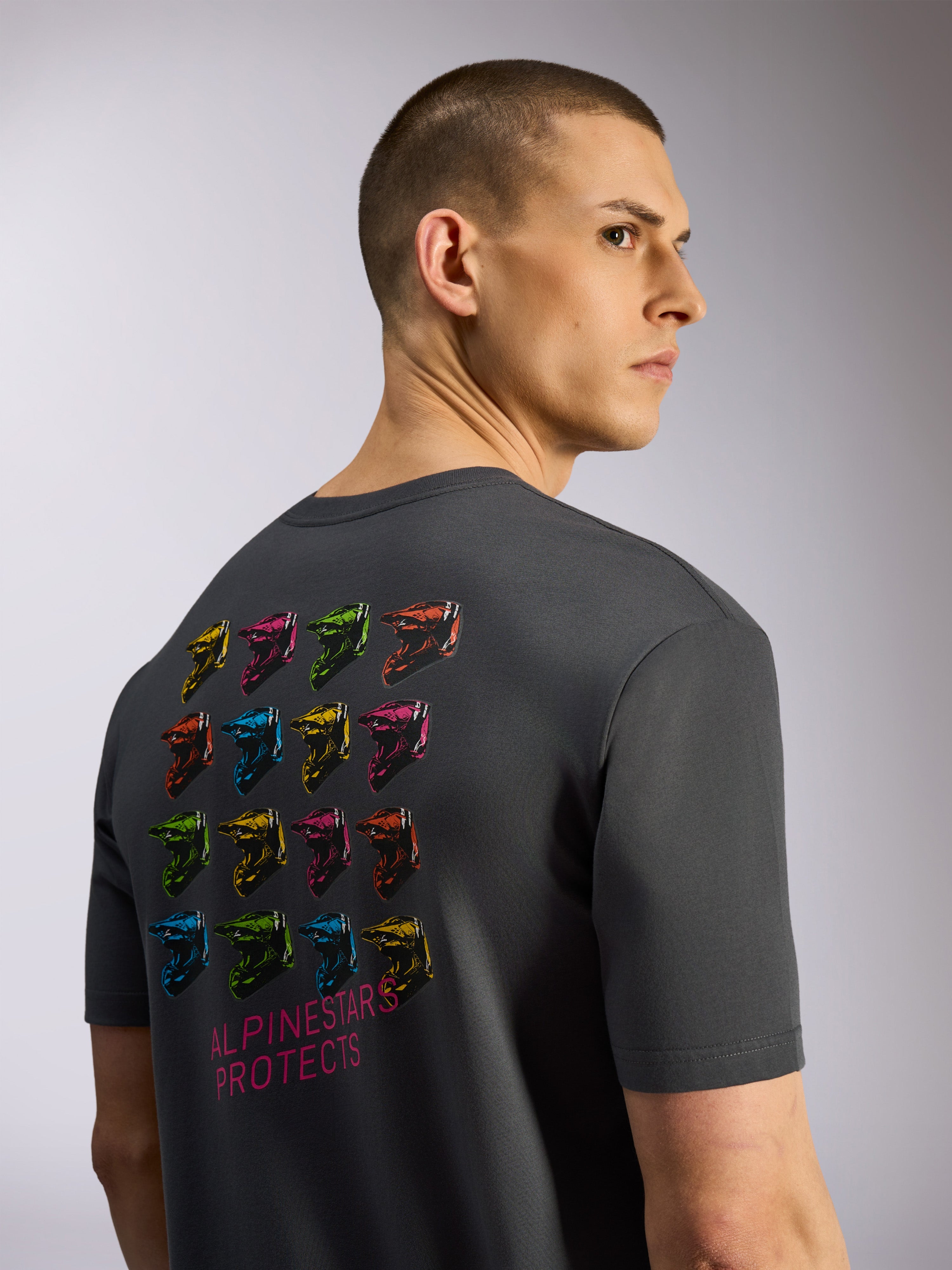 Alpinestars Pop Helmet CSF Tee, Short Sleeve T-Shirt, Charcoal Gray, Back View featuring Grid of Colorful M10 Helmets and 'Alpinestars Protects' Text, Casual Motorsport Streetwear