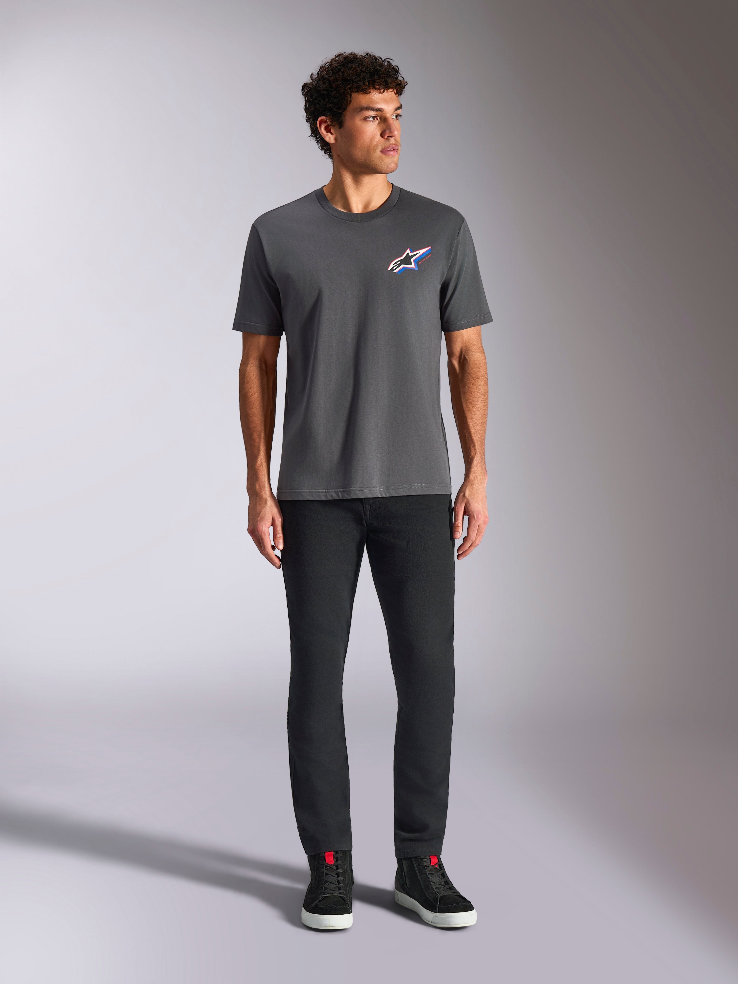 Alpinestars Angler CSF Tee, Short Sleeve T-Shirt, Charcoal, featuring a vibrant multi-color Astars logo on the chest, worn by a model with black pants and sneakers, Casual Motorsport Streetwear