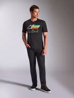 Alpinestars Trifecta CSF Tee, Short Sleeve T-Shirt, Black, featuring a white Astars logo with cyan, yellow, and orange stripes and 'Racing Ahead' text, worn by a model with black pants and sneakers for casual motorsport streetwear