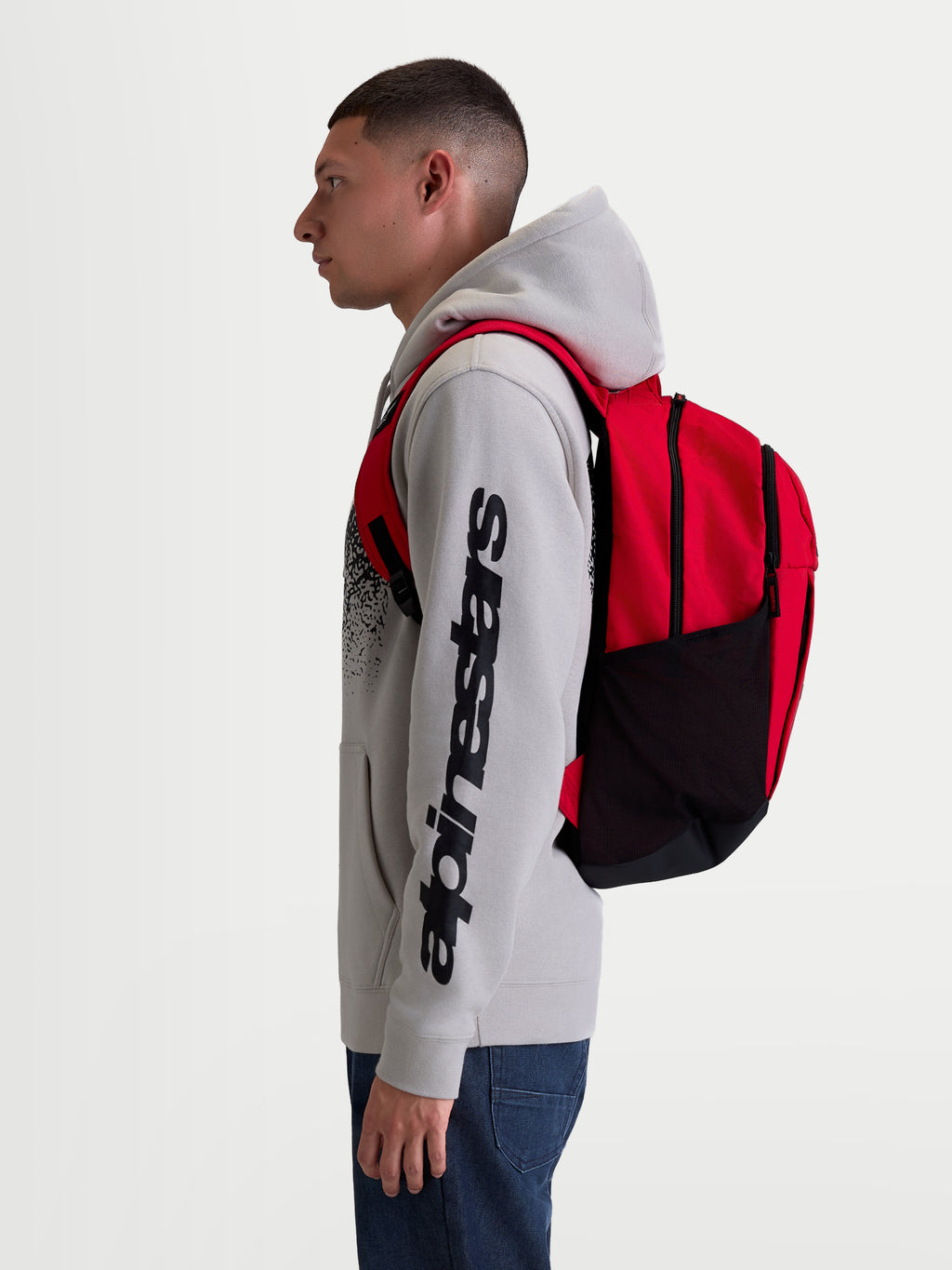Alpinestars GFX Boss Backpack, Red and Black 20L Sportswear Daypack, durable 600D polyester with side mesh water bottle pockets and padded air mesh shoulder straps, shown on-model for urban commuting and daily use.