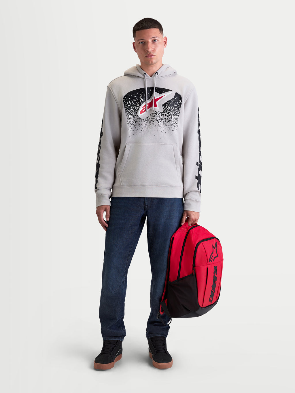 Alpinestars GFX Boss Backpack, Red and Black Sportswear Daypack, 20L capacity, durable 600D polyester with raised silicone Astars logo, held by a male model for casual urban commuting.