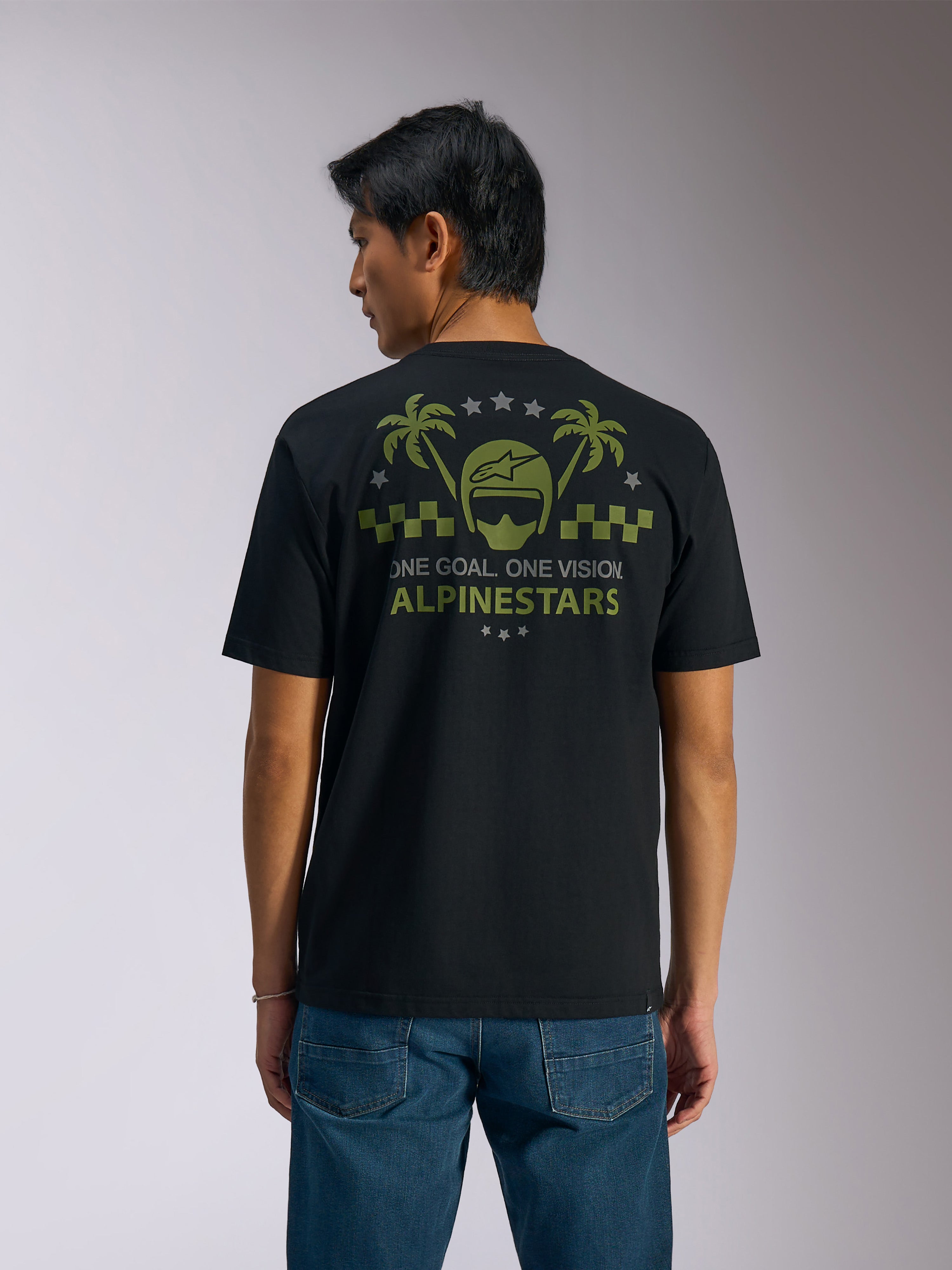 Alpinestars Order CSF Tee, Short Sleeve T-Shirt, Black, Back View, Olive Green Graphic with Palm Trees and Helmet Logo, 'ONE GOAL. ONE VISION. ALPINESTARS' text, paired with blue jeans, casual motorsport streetwear