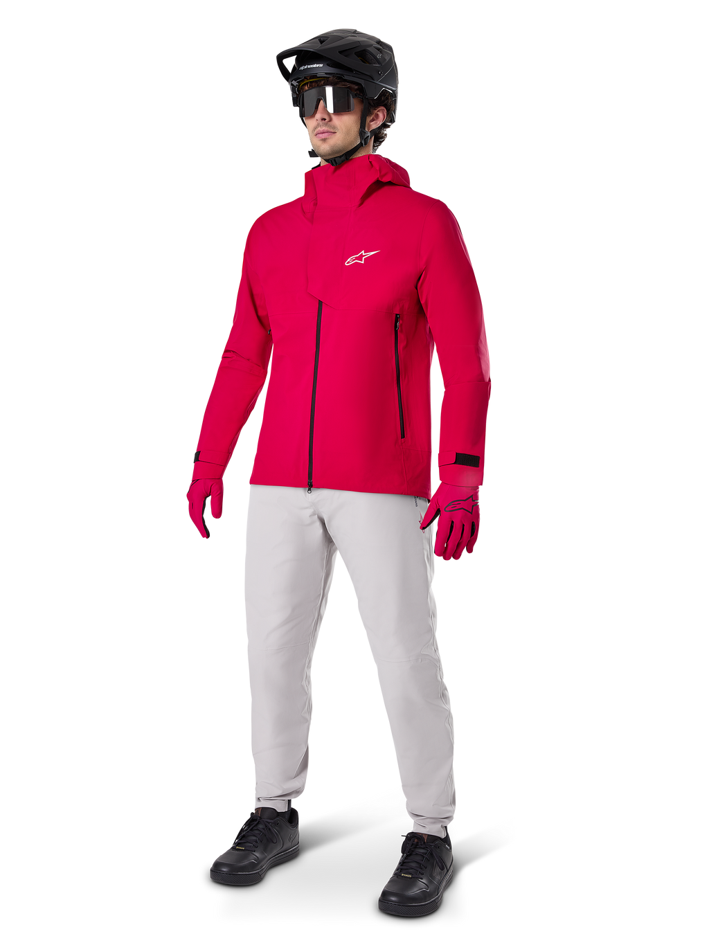 Male cyclist wearing the Alpinestars A-Dura Elite Waterproof Jacket in Red Fluo, paired with light grey technical pants, red gloves, black MTB helmet with goggles, and black shoes, complete high-performance outfit for mountain biking