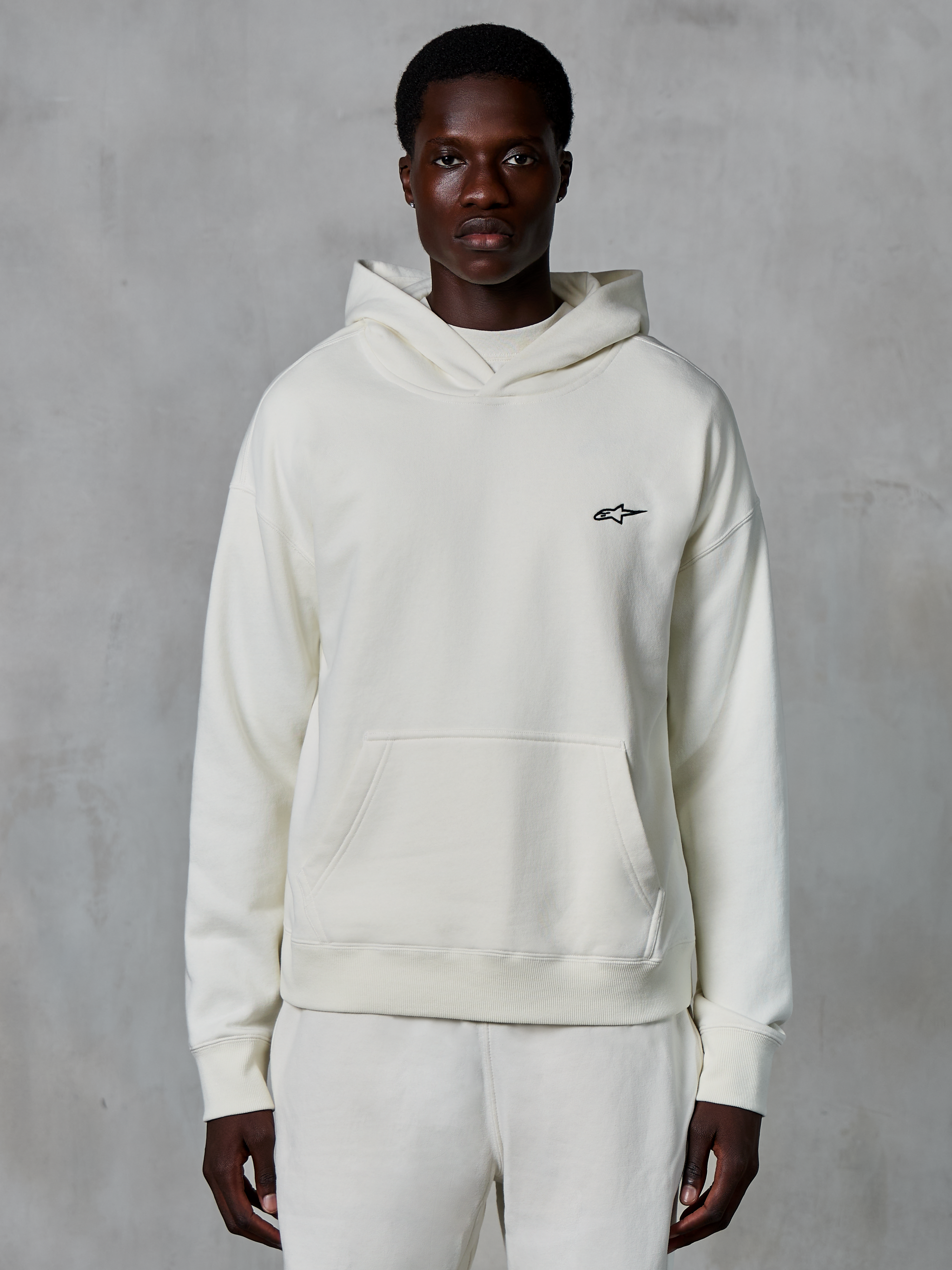 Alpinestars Essentials Ageless Hoodie, off-white, worn by male model, small black logo on chest, front pouch pocket, long sleeves, casual motorsport-inspired streetwear