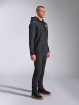 Alpinestars Formulation Hoodie, casual zip-up poly fleece, Black, featuring a white chest logo and drawstring hood, worn with black pants and black sneakers, full body side profile, motorsport-inspired streetwear.