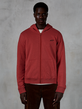 Alpinestars Essentials Ageless Zip Hoodie, Brick red full-zip hooded sweatshirt, worn by model with brown corduroy pants, featuring a small black logo on the chest, relaxed fit casual streetwear