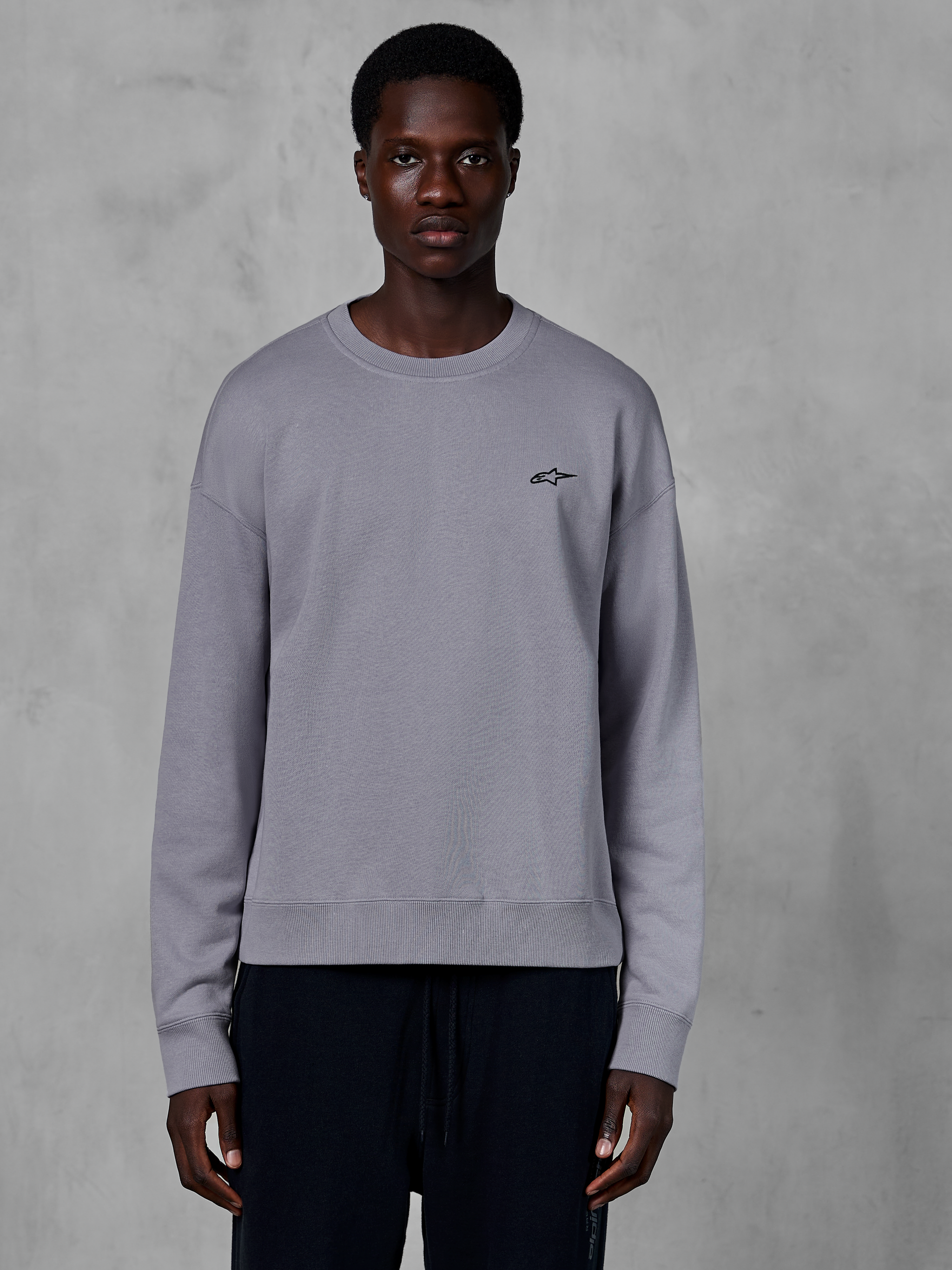 Alpinestars Essentials Ageless Crew, Silver crewneck sweatshirt worn by a model, featuring a small black star logo on the chest, relaxed fit with ribbed cuffs and hem, casual motorsport streetwear