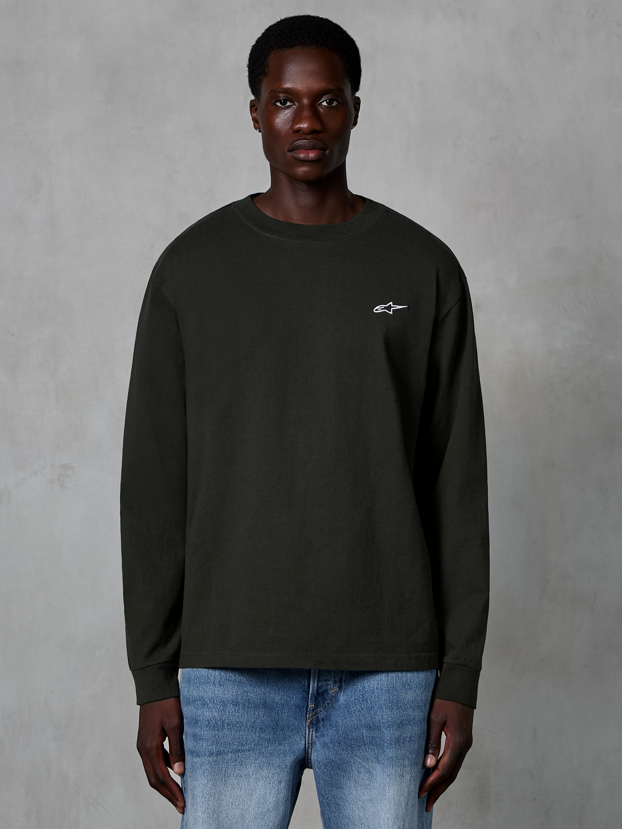Alpinestars Essentials Ageless LS Tee, Long Sleeve T-Shirt, Off Black, featuring a small white Alpinestars logo on the chest, worn by a model with blue jeans, casual organic cotton streetwear