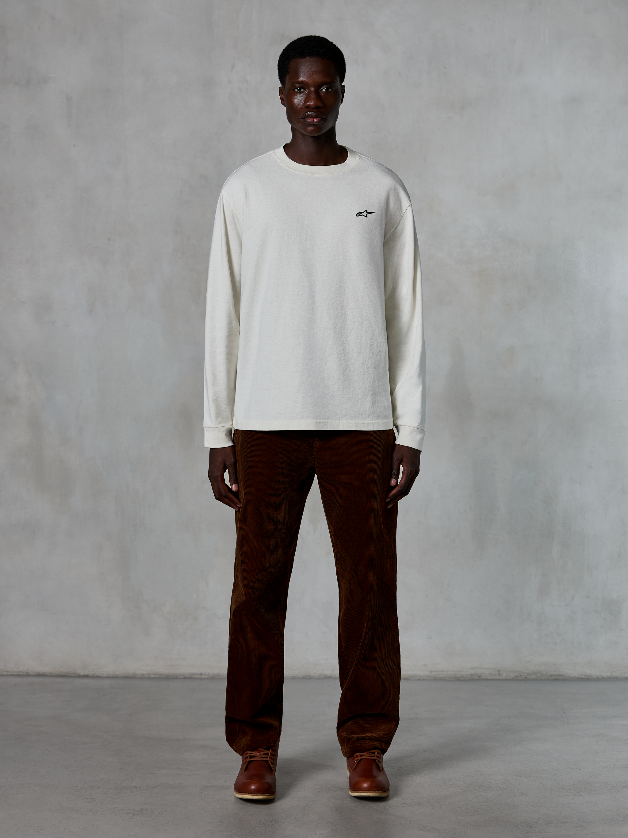 Alpinestars Essentials Ageless LS Tee, Long-Sleeve T-Shirt, Off-White, worn by model with brown corduroy pants and brown leather boots, featuring a small black logo on the chest, relaxed contemporary fit, casual lifestyle streetwear