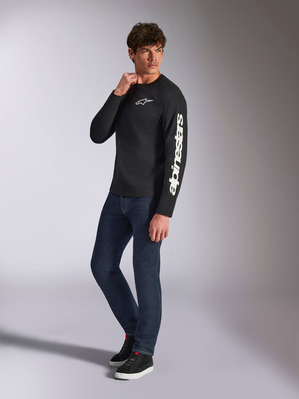 Alpinestars Trackside CSF Tee, Long Sleeve T-Shirt, Black, white vertical Alpinestars branding on sleeve and chest logo, worn by male model with dark blue jeans and sneakers, casual motorsport streetwear