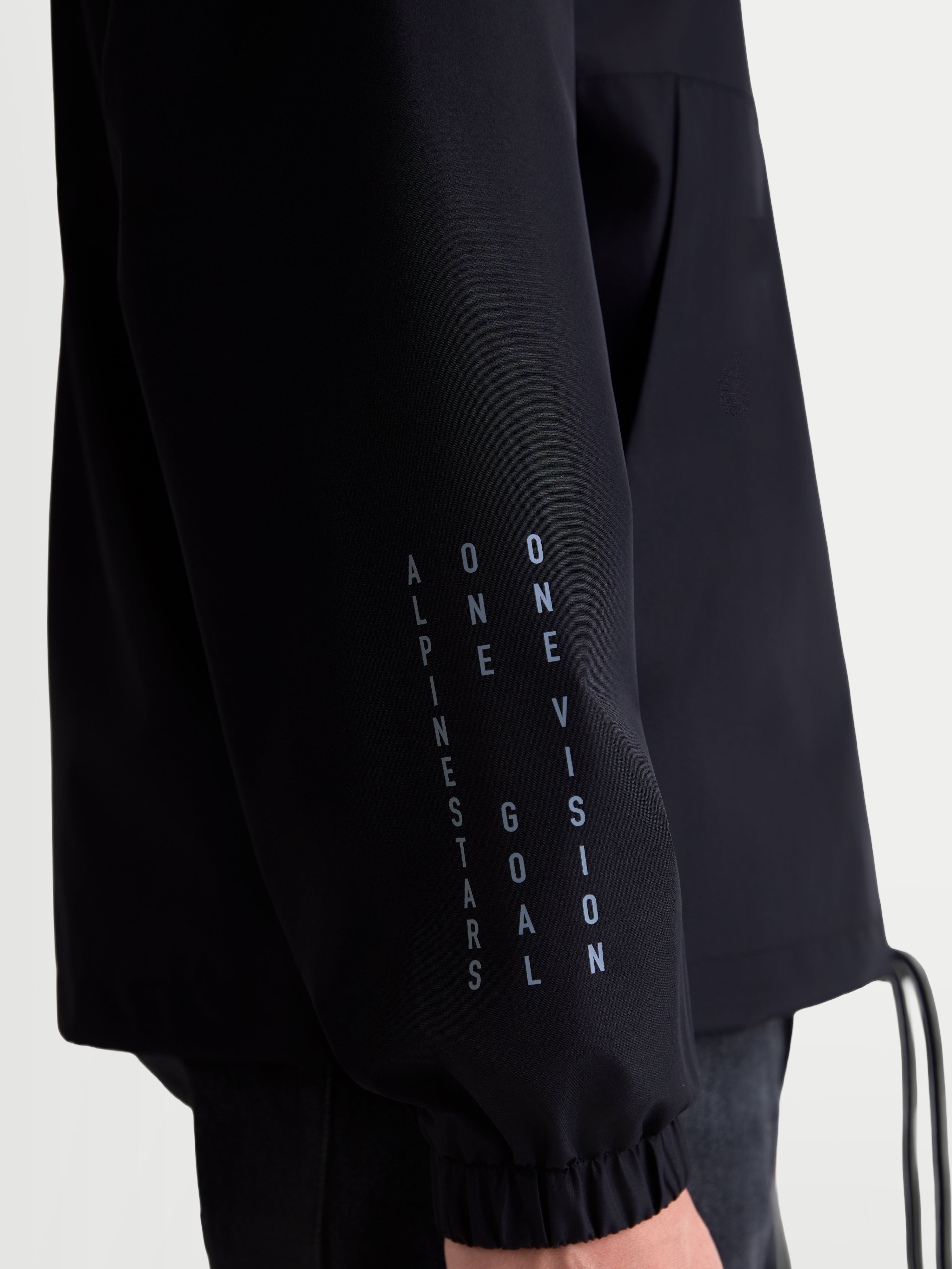 Alpinestars Speeder Resolve Windbreaker Jacket, Black Lightweight Sportswear Jacket, close-up view of sleeve featuring vertical branding and elastic cuff, windproof 100% polyester construction for urban use.