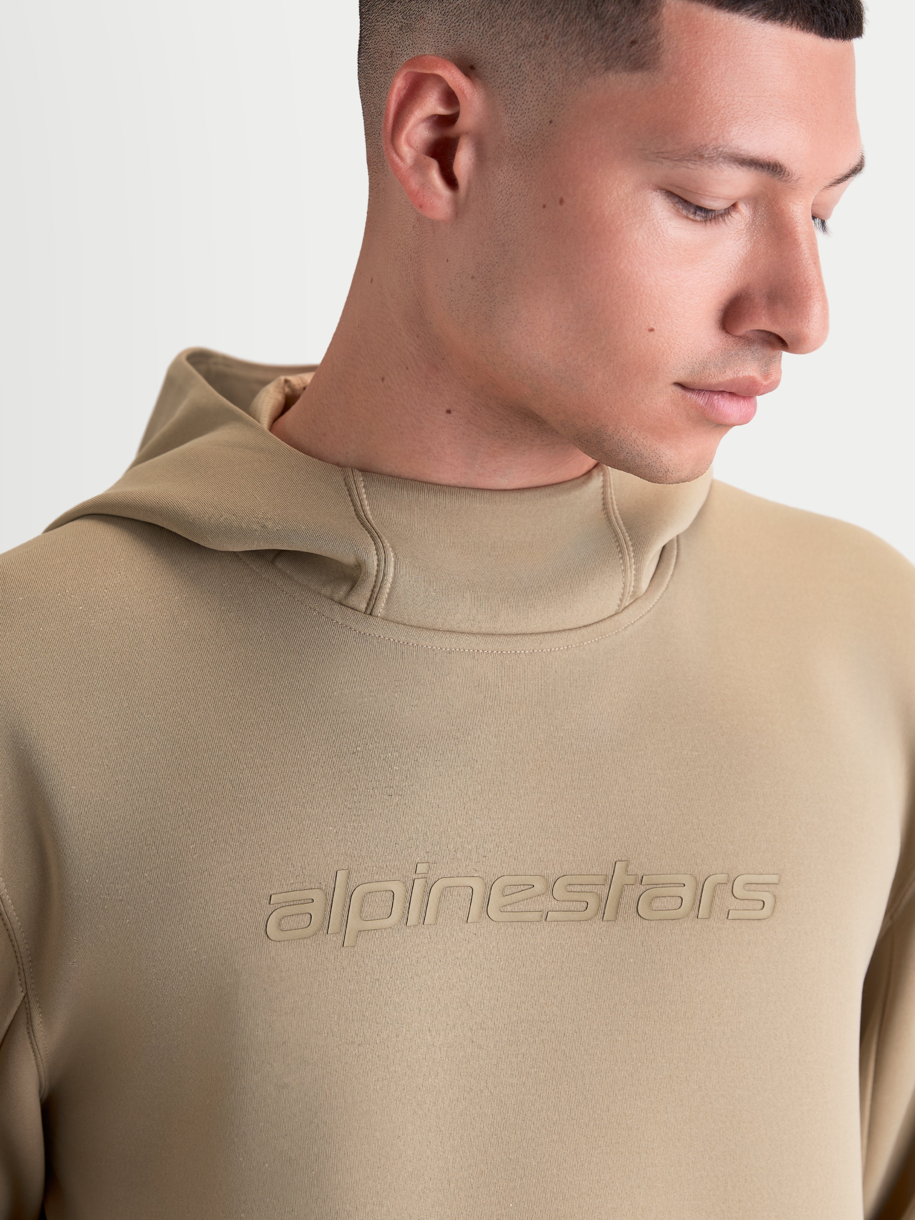 Alpinestars Datrix Hoodie, Sportswear Pullover Hoodie, Unisex, Putty Brown, featuring tonal HD Alpinestars branding, mesh-lined hood, and tri-blend double-face fleece construction, close-up view on model.