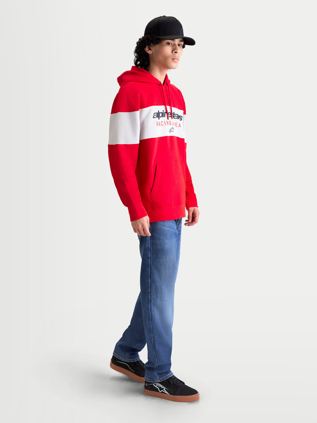 Alpinestars Cubic Hoodie, Men's Sportswear Pullover Fleece in Red and White, featuring a color-blocked design and bold Alpinestars word logo on the chest. On-model side view showing the drawstring hood, front pouch pocket, and ribbed cuffs for casual off-bike comfort.