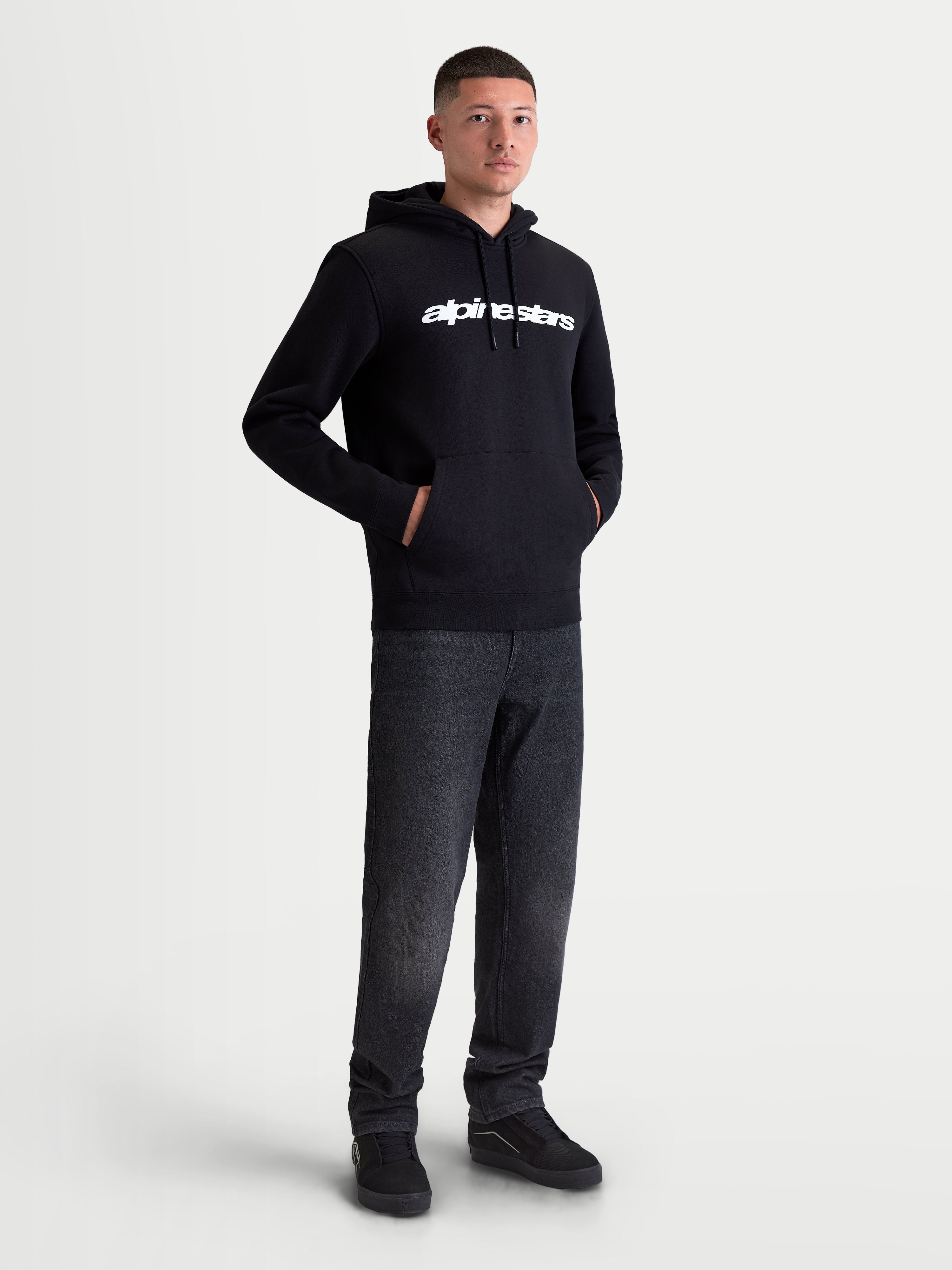 Alpinestars Race Wordmark Hoodie, Men's Sportswear Pullover Fleece, Black and White, featuring a bold white linear chest logo, self-lined hood with drawstrings, and a front pouch pocket. Constructed from a comfortable cotton and recycled polyester blend for everyday casual wear, shown on model.