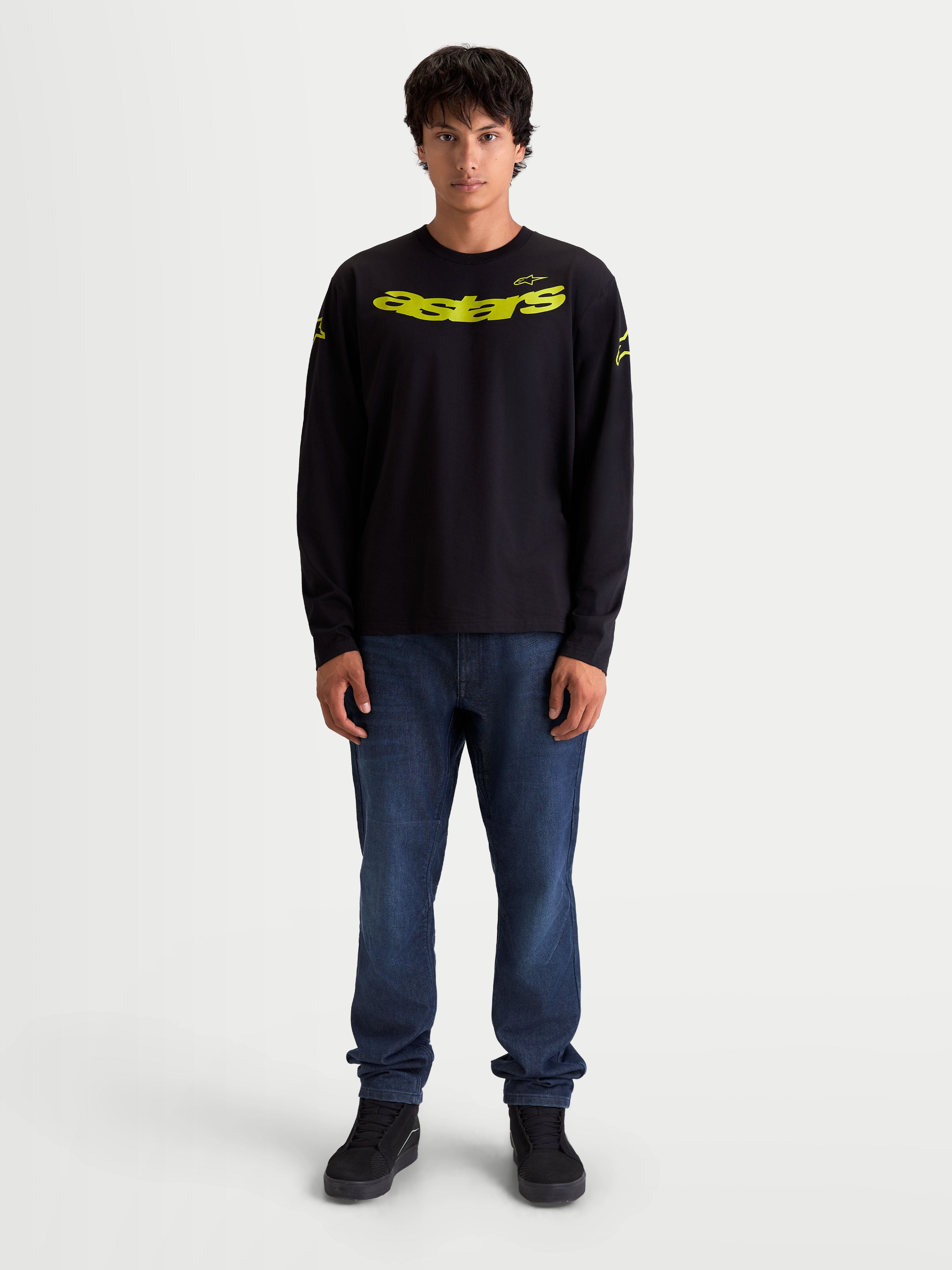 Alpinestars Velocifier CSF Tee, Long Sleeve Sportswear, Black and Yellow, On-Model. This unisex cotton-blend long sleeve t-shirt features a vibrant yellow curved Astars front graphic, matching shoulder logos, and rib cuffs, designed for daily casual wear with a motorsport-inspired aesthetic.