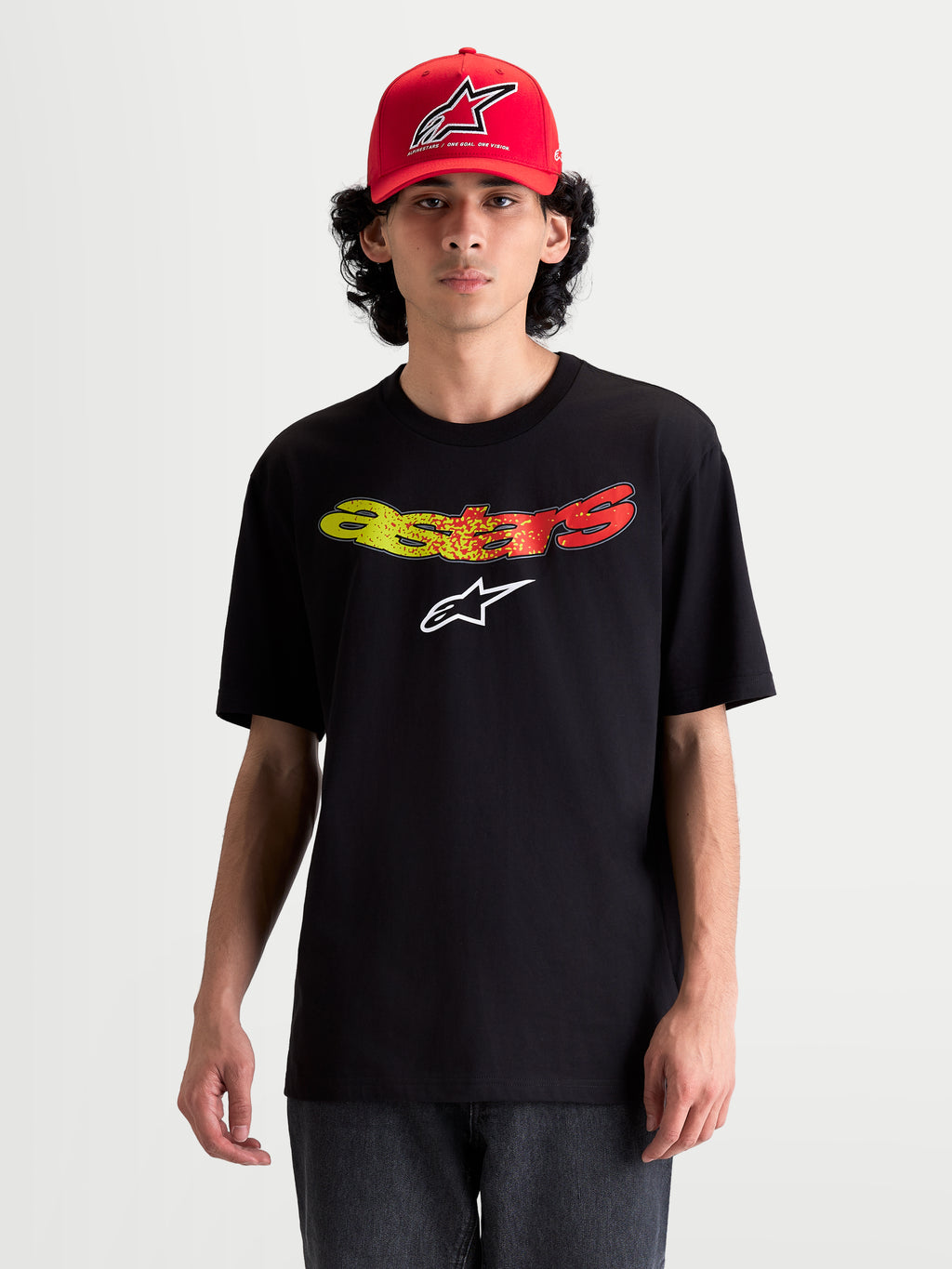Alpinestars Elliptogrit CSF Tee, Short Sleeve Sportswear T-shirt on model, Black with curved Astars wordmark in Red and Yellow gradient graphics, soft cotton-poly blend, casual everyday wear.
