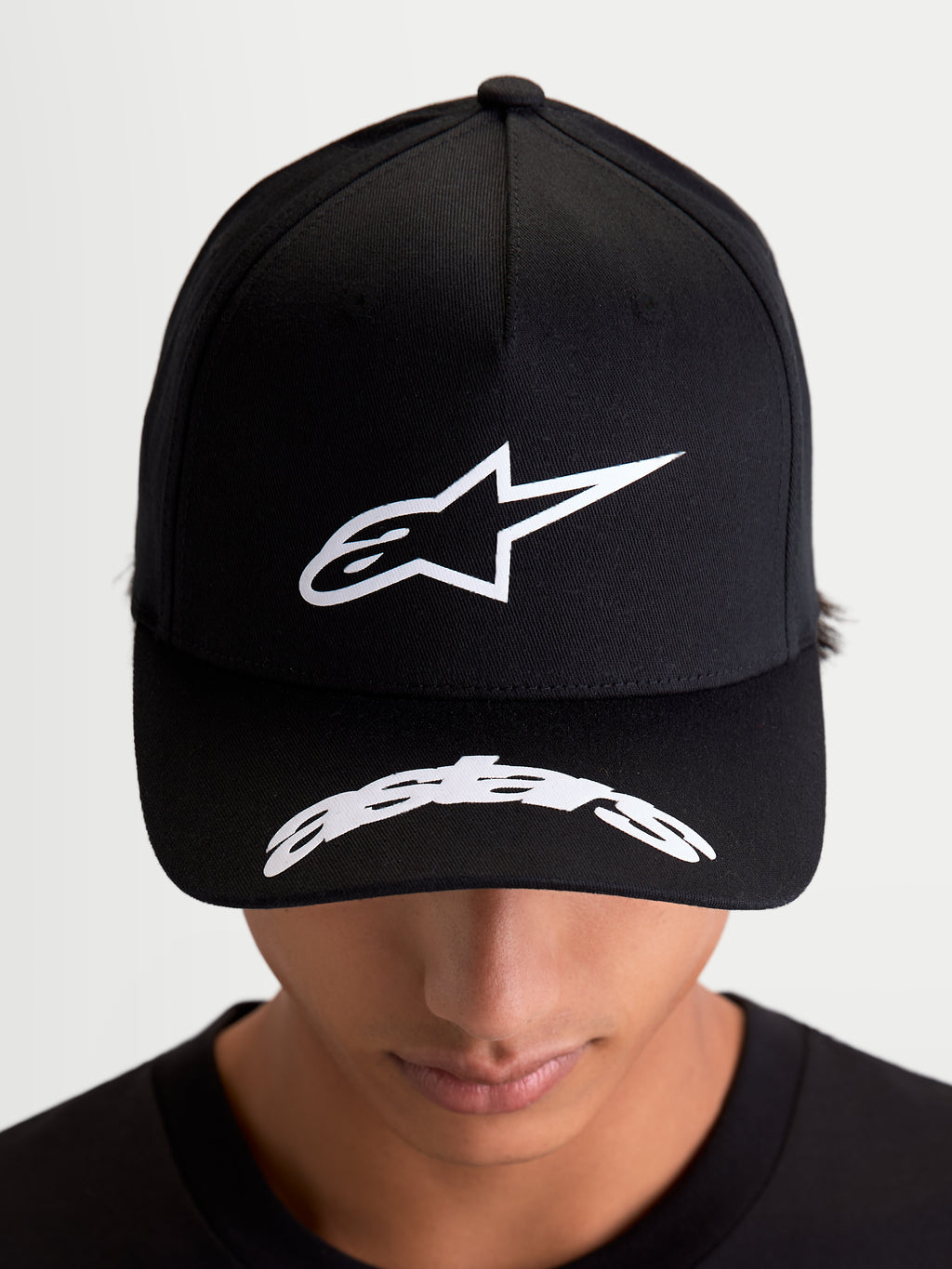Alpinestars Arclight Hat, Black Sportswear Baseball Cap, on-model front view showing white puff-print Astars logo on a structured crown and curved word logo on the bill, motorsport-inspired casual wear.