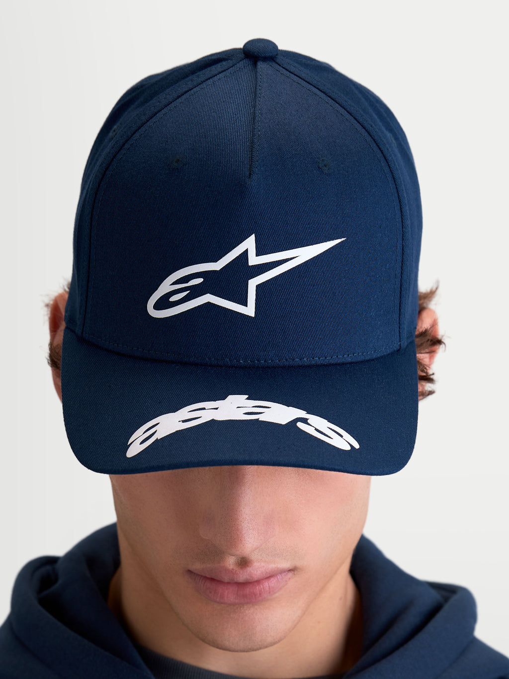 Alpinestars Arclight Hat, Motorsport-inspired Sportswear Baseball Cap for Men and Women, Navy Blue and White, featuring a structured crown with a textured puff-print Astars logo, curved bill with Astars wordmark detailing, durable cotton twill construction, on-model front view.