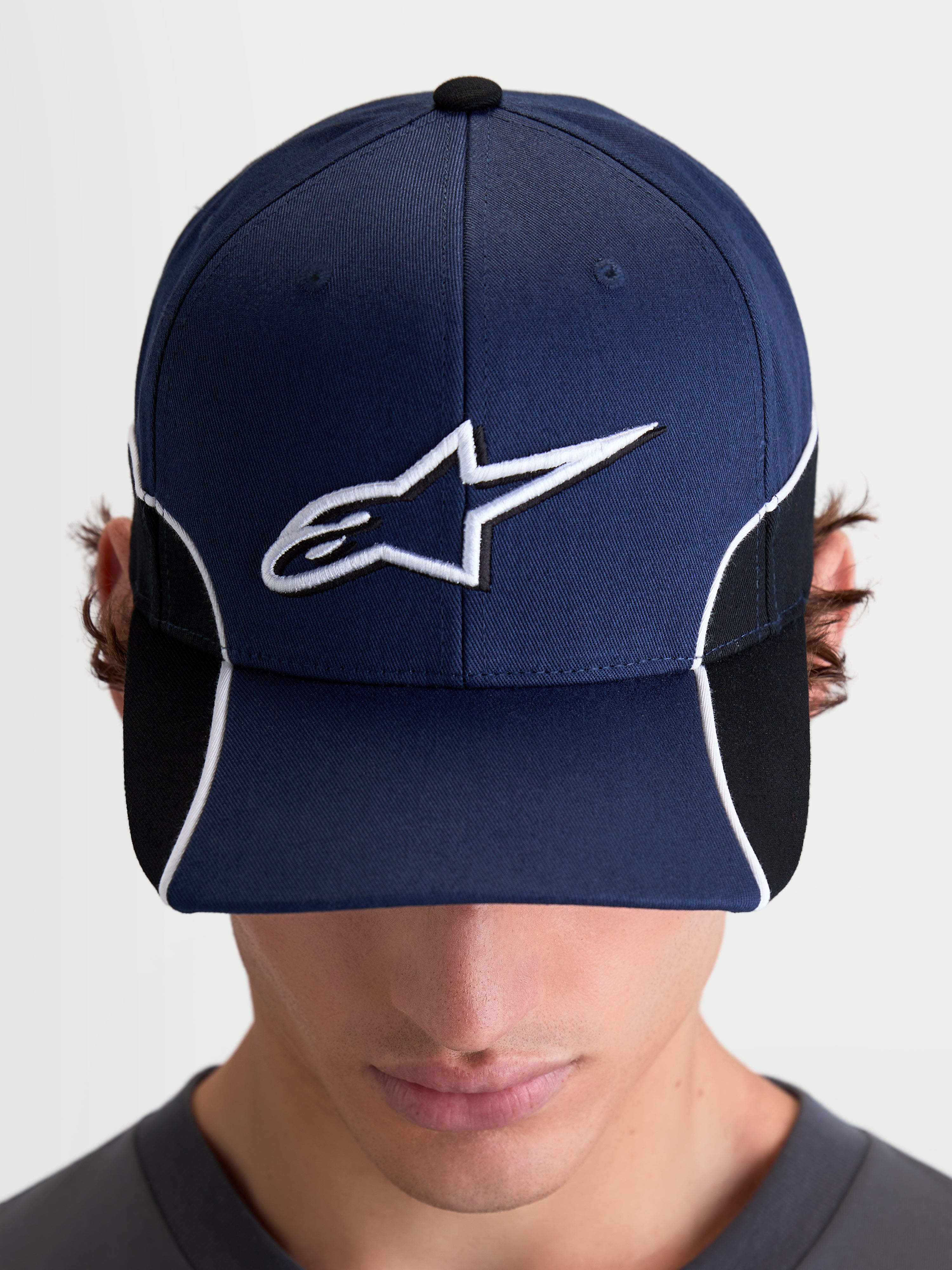 Alpinestars 500 Snapback Hat, Motorsport-Inspired Sportswear Cap, Unisex, Navy Blue and Black, featuring a curved bill and 3D embroidered white Astars logo with contrast piping and cut-and-sew detailing, front view on model.