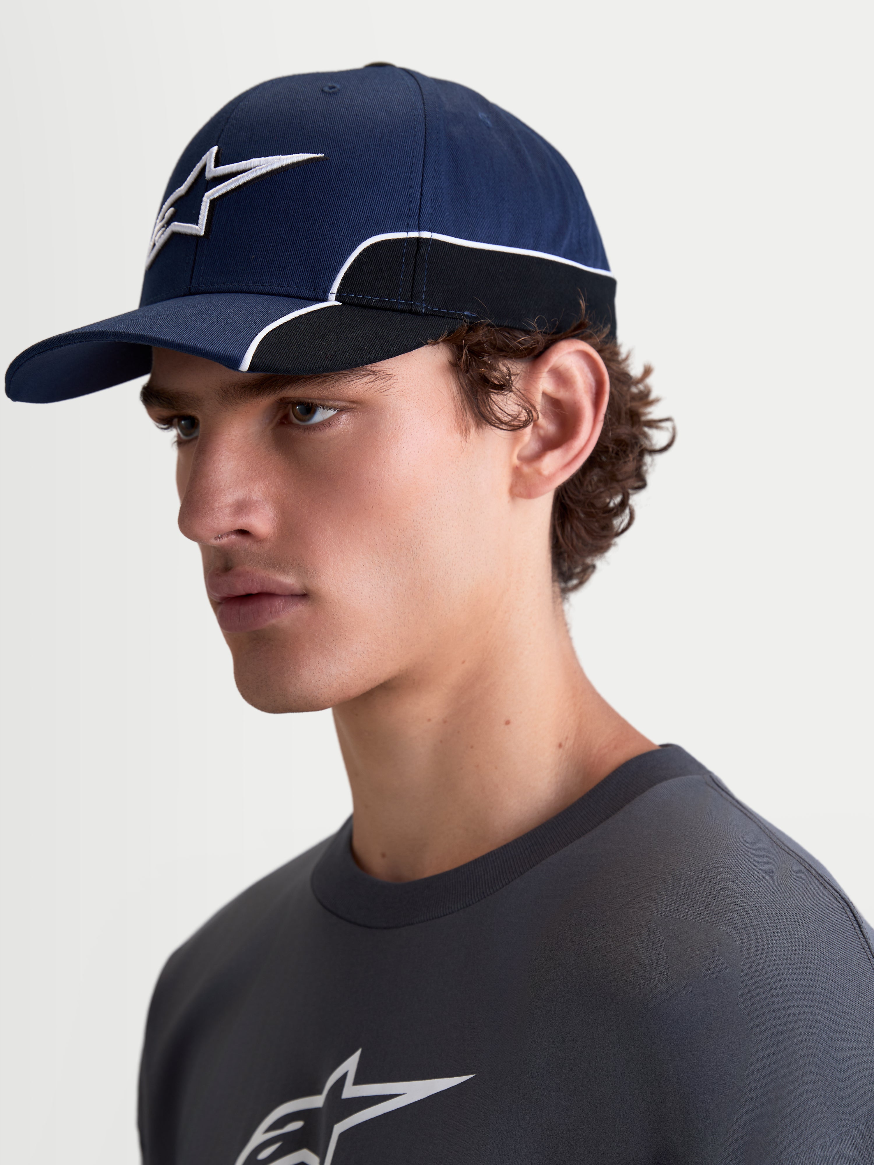 Alpinestars 500 Snapback Hat, Sportswear Baseball Cap, Unisex, Navy Blue and Black, Durable Cotton Twill, features curved bill and 3D Astars logo embroidery with white contrast piping, on-model side view.