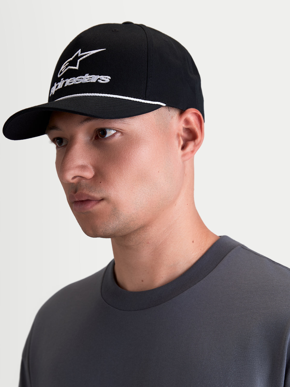 Alpinestars Combo Logo Snapback Hat, Black and White Sportswear Lifestyle Cap, featuring a curved bill, structured crown, white Alpinestars combo logo embroidery and rope trim detail, shown on-model in a profile view.